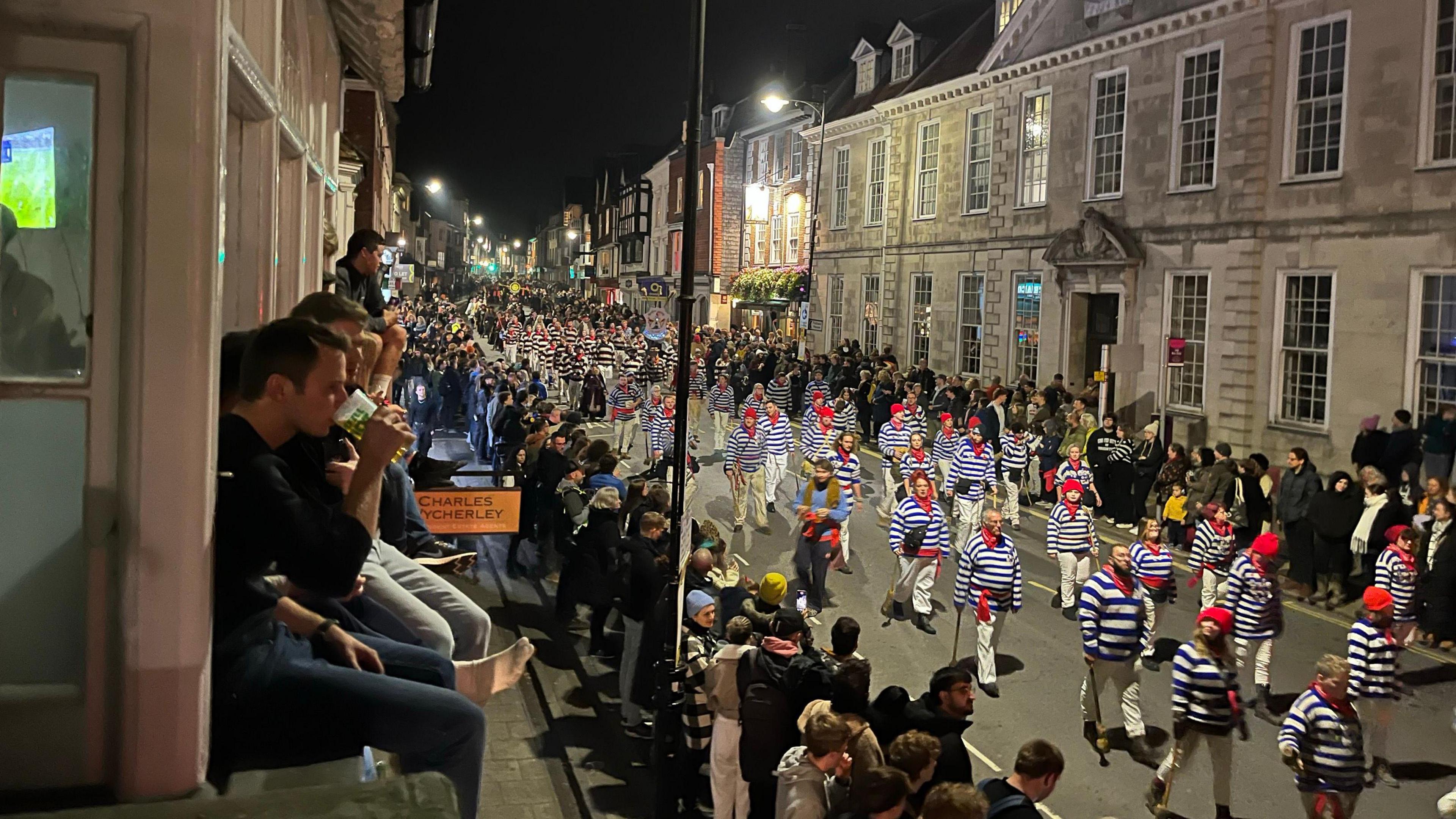 Spectators perched on a window sill looking out over Lewes Bonfire procession in High Street, Lewes