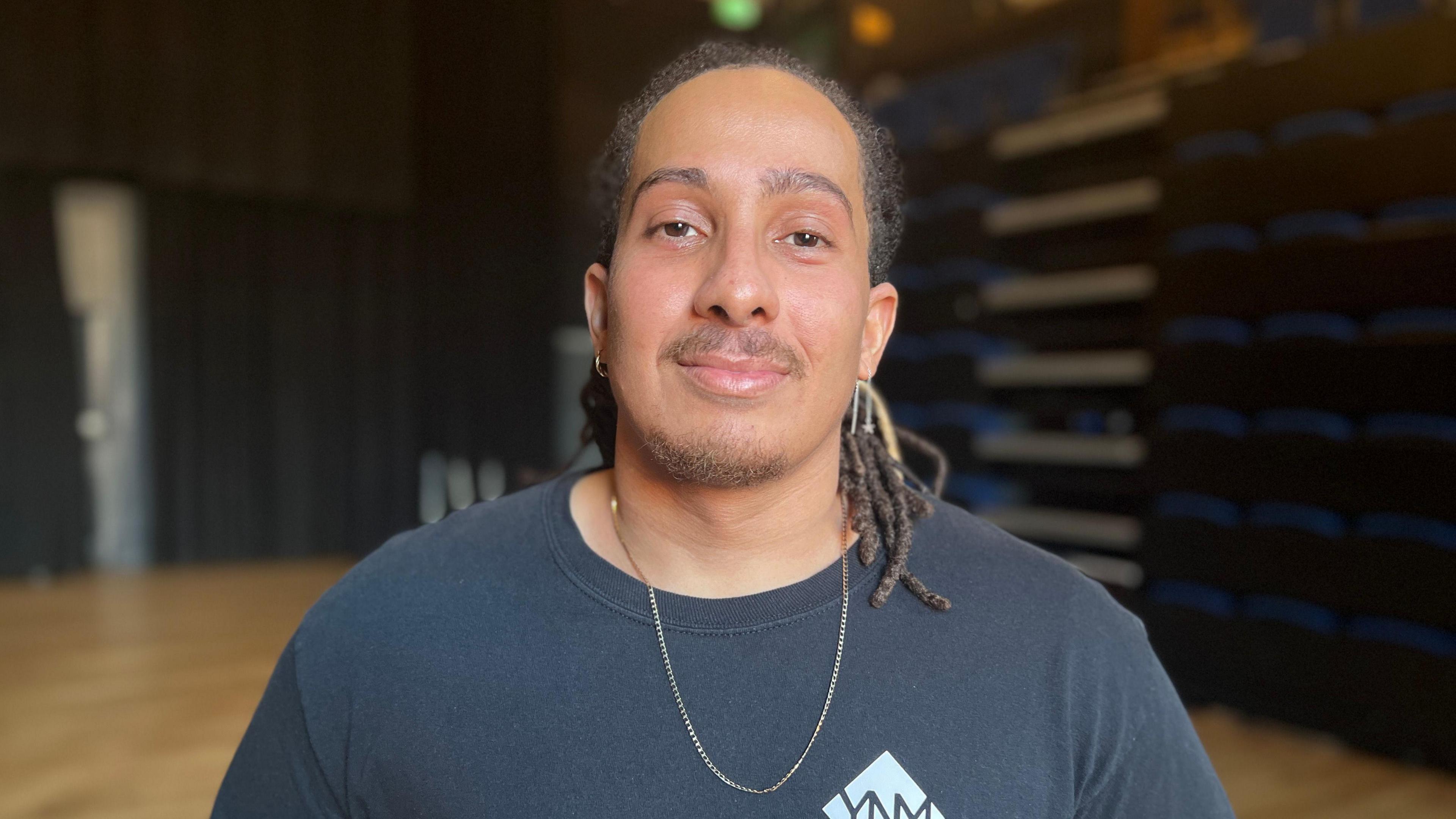 A portrait picture of Tyler Attwood, Founder of Your Next Move. He is smiling at the camera, wearing a black long-sleeved top and a gold chain. 