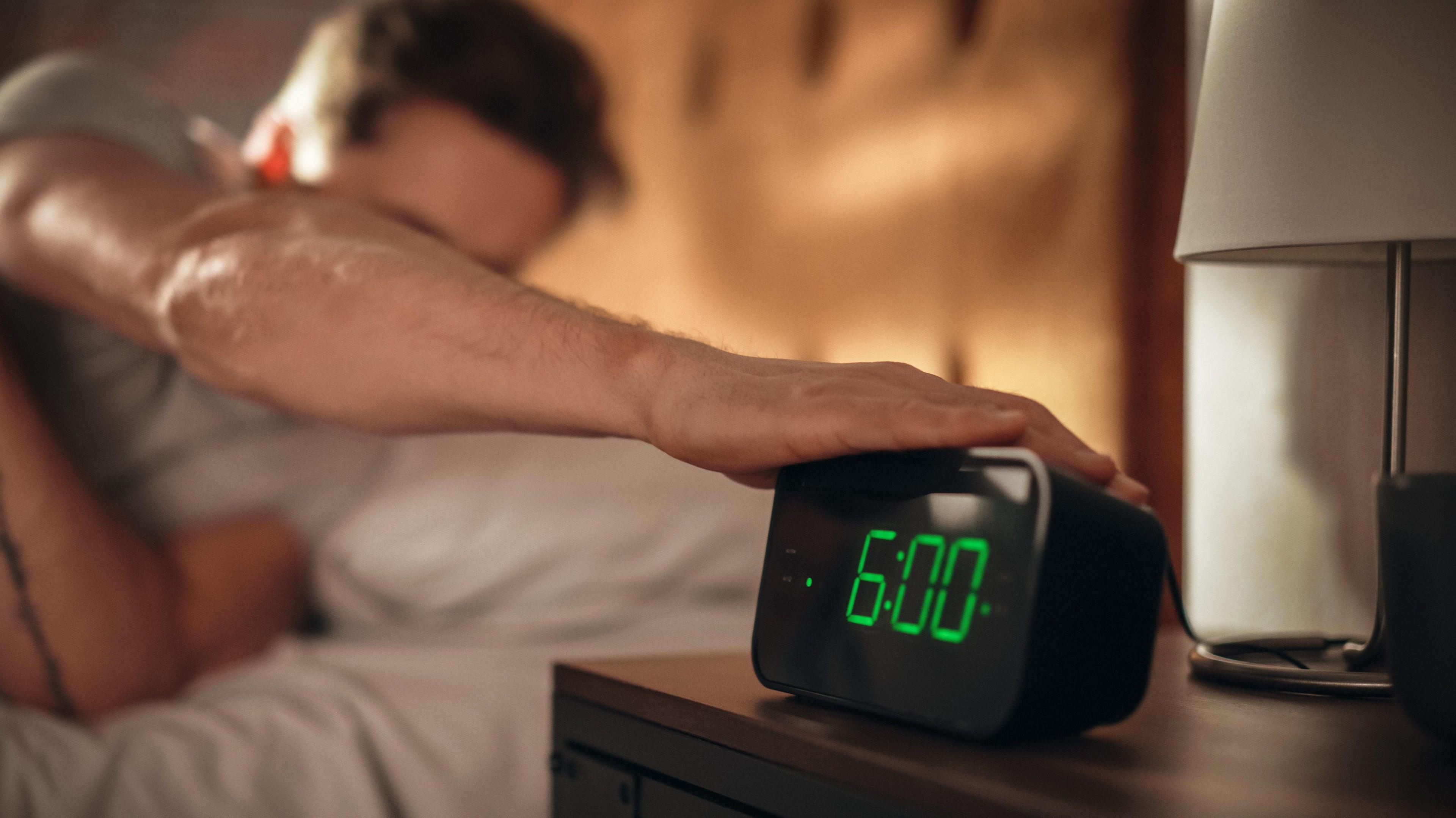 Man in bed reaching over to his radio alarm clock