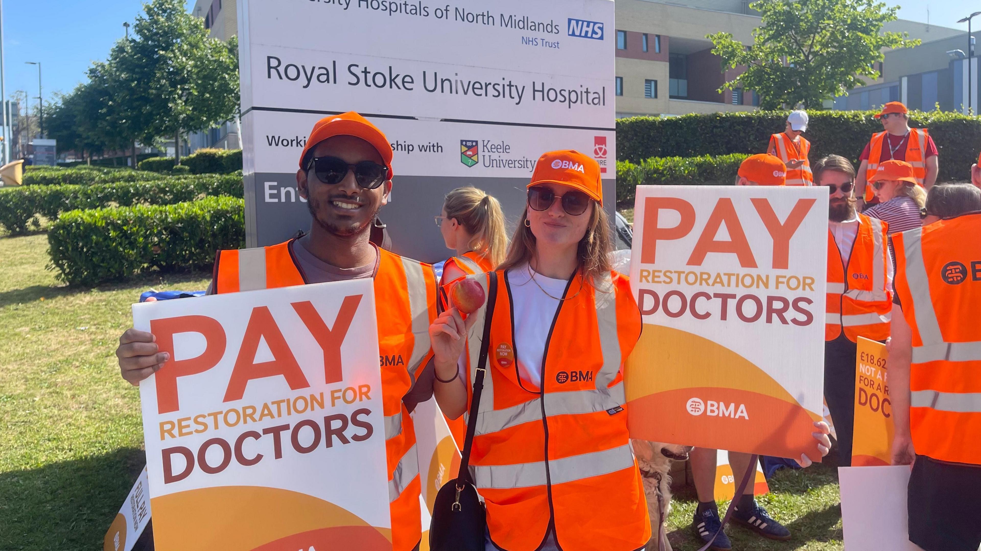 A male and female doctor stand on a picket line outside a hospital
