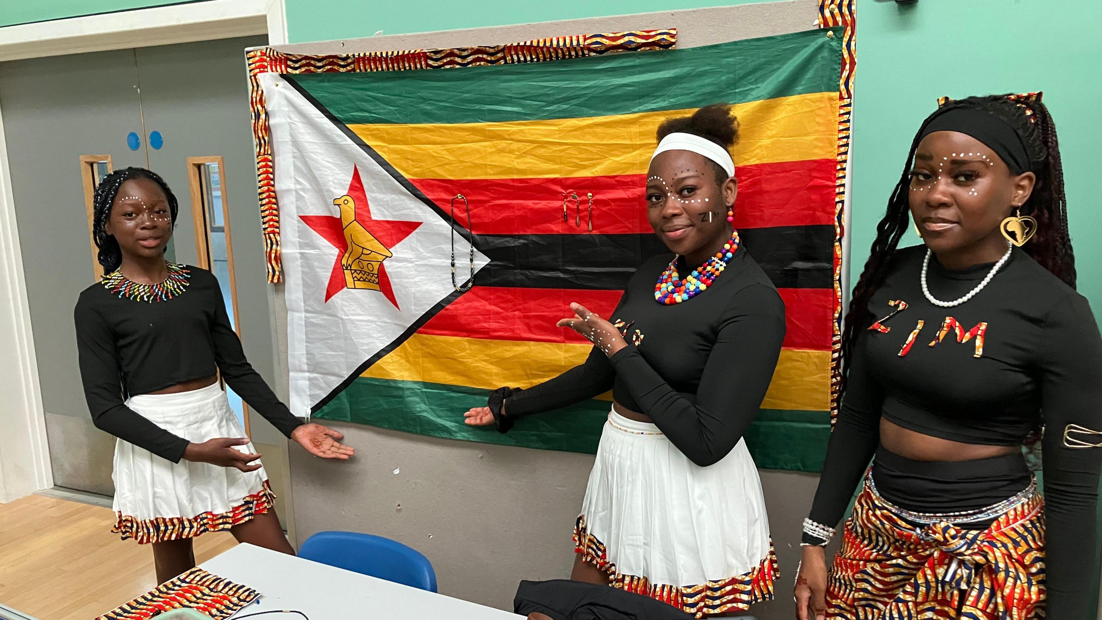 Three girls dressed in the Zimbabwean traditional clothes holding the Zimbabwe flag 