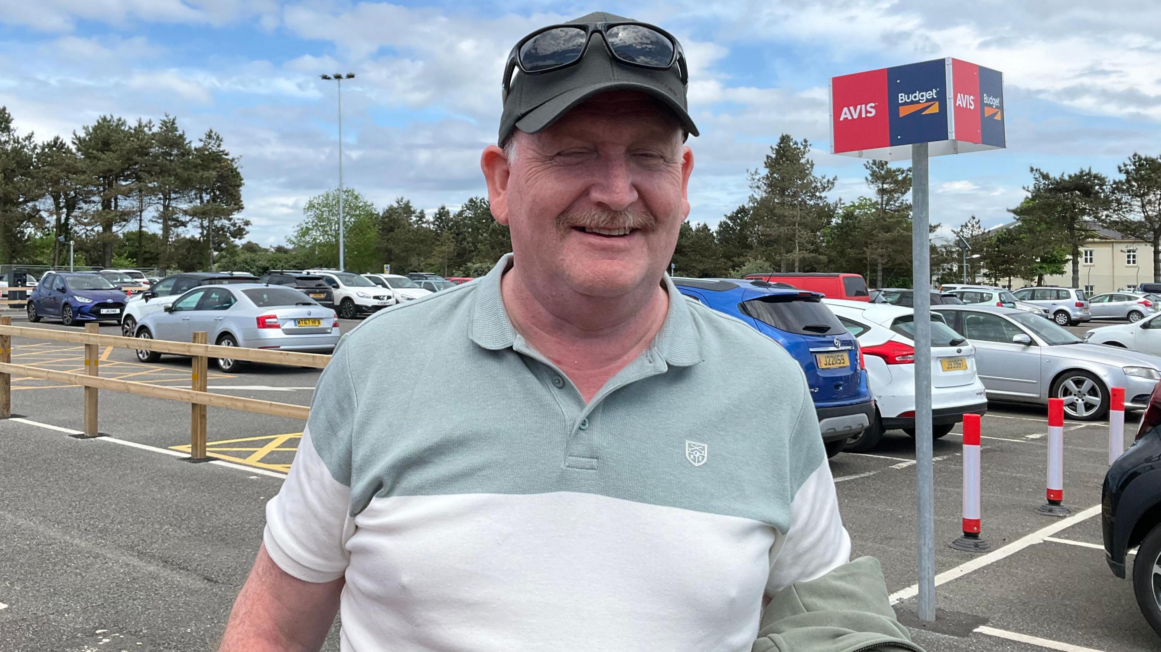 Stephen Chapman, wearing a cap, stands in Jersey Airport car park.