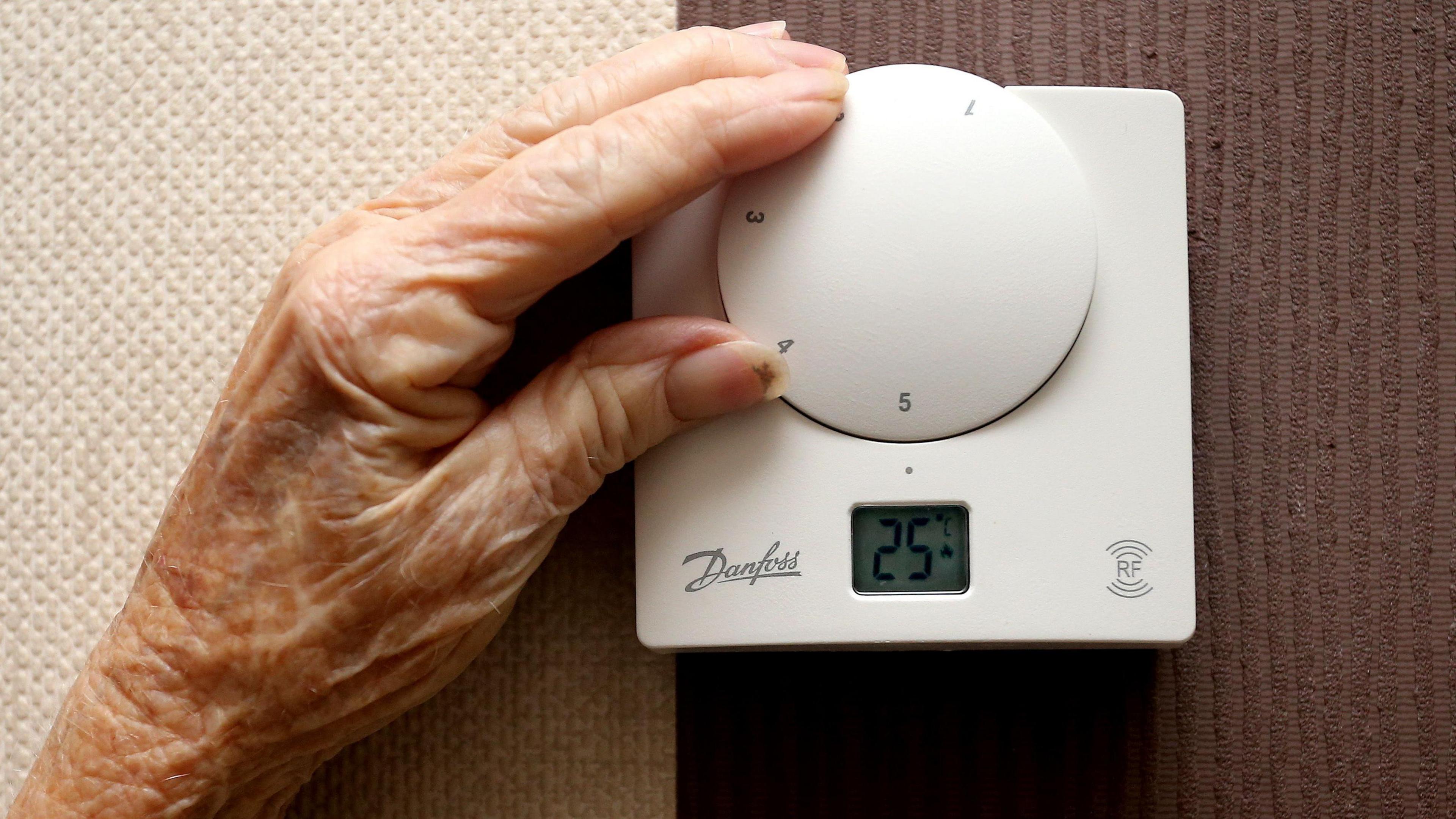 The hand of an elderly person is adjusting a thermostat to 25 degrees Celsius.