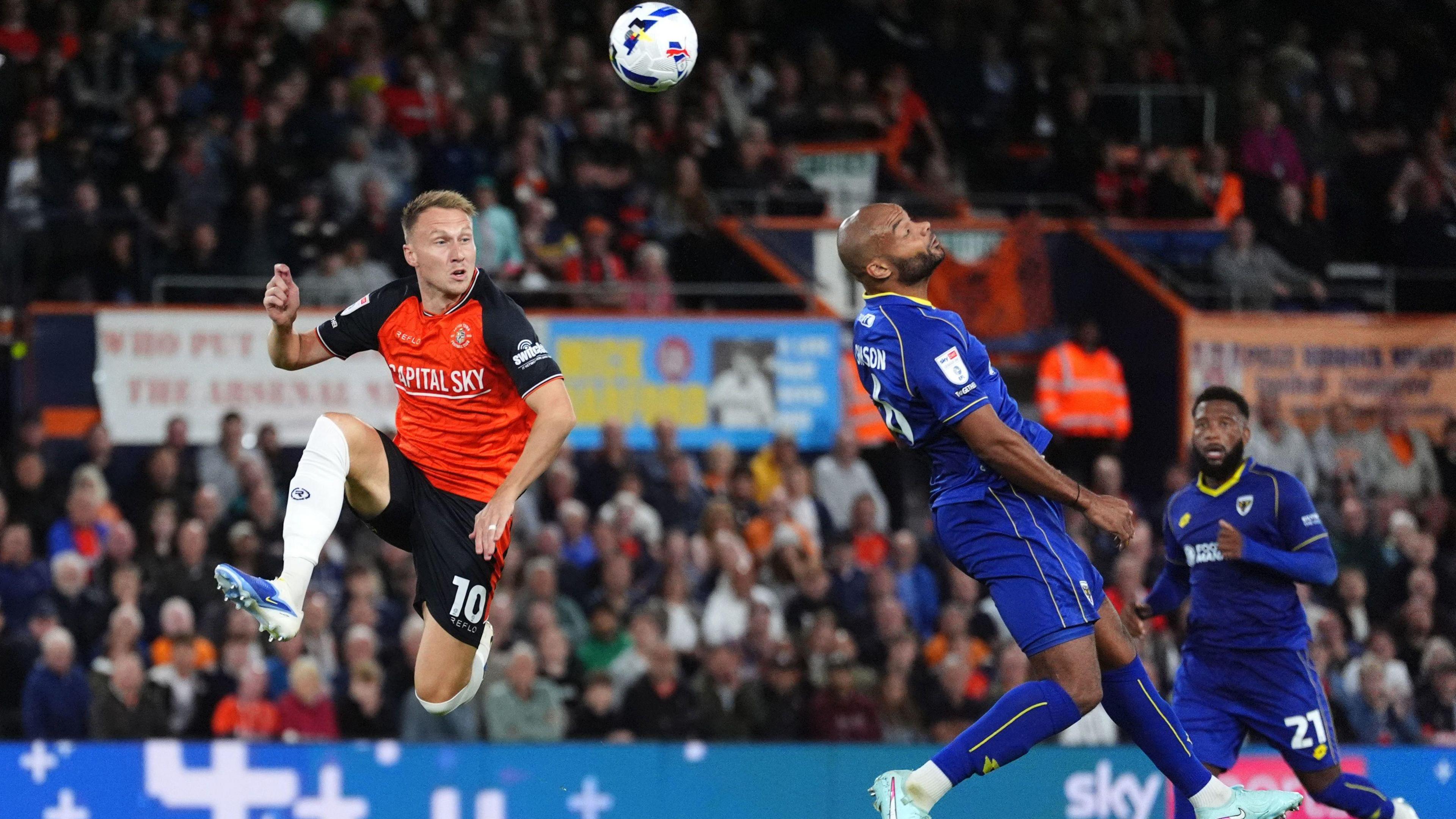 Ryan Johnson heads the ball up and over under pressure from Luton attacker Cauley Woodrow, before the balls lobs Wimbledon goalkeeper Nathan Bishop for an own goal