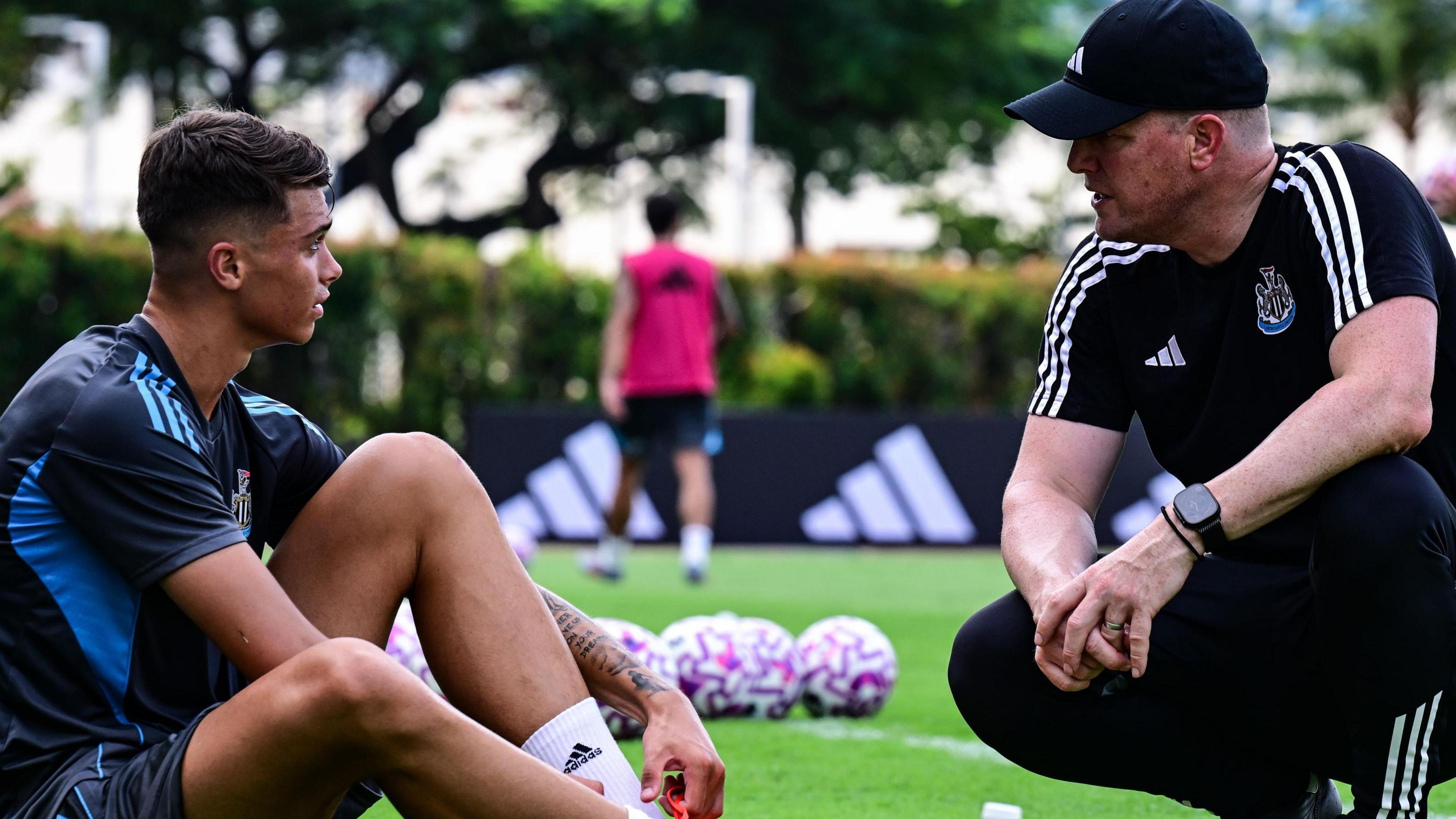Lewis Miley sits on the pitch as Eddie Howe crouches down opposite him to talk