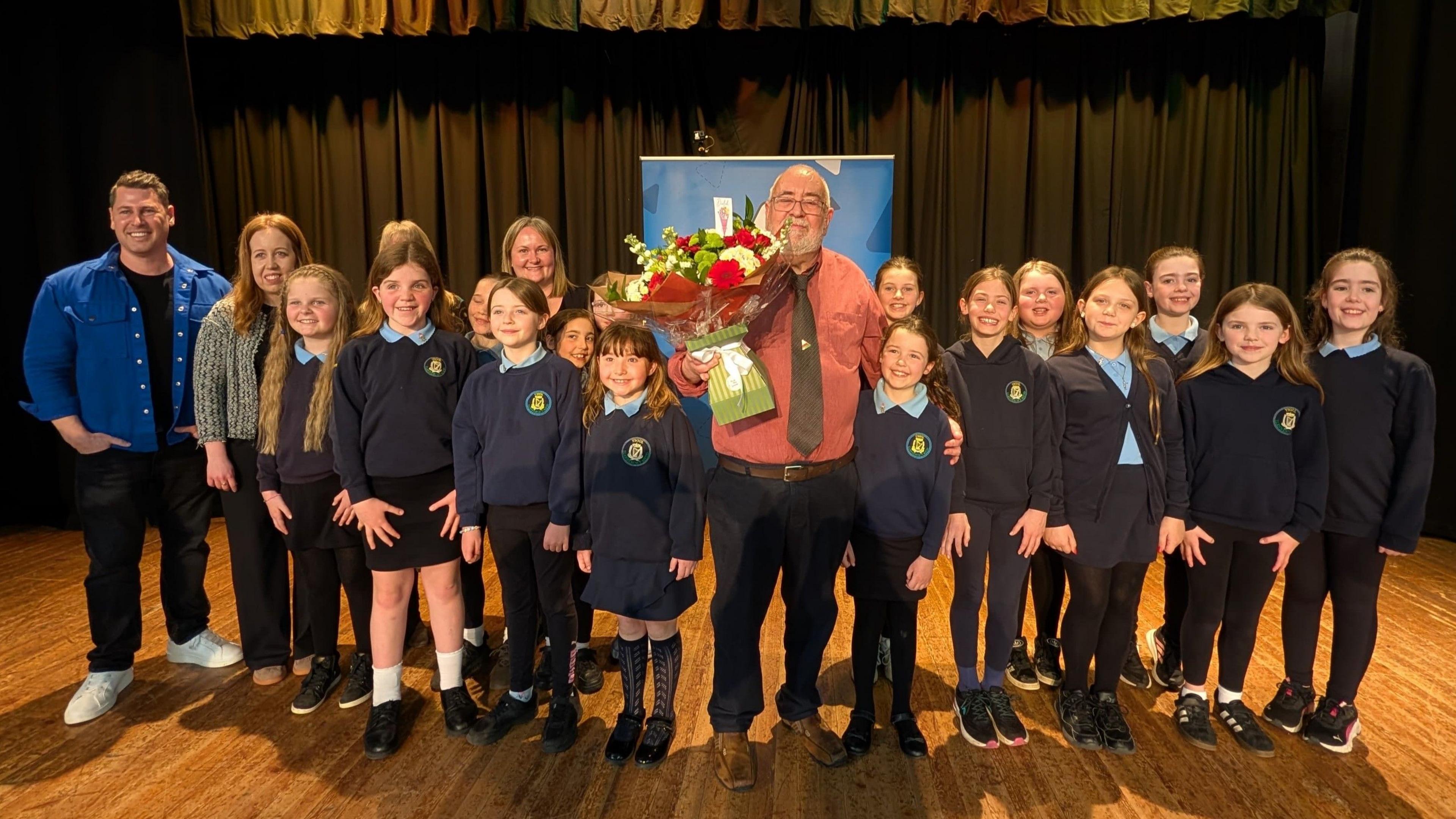 Derek Evans, enillydd Tlws John a Ceridwen Hughes, Uwchaled 2026 (gyda disgyblion Ysgol Gynradd Llanerchymedd, ei deulu, a chyflwynydd S4C Alun Williams)