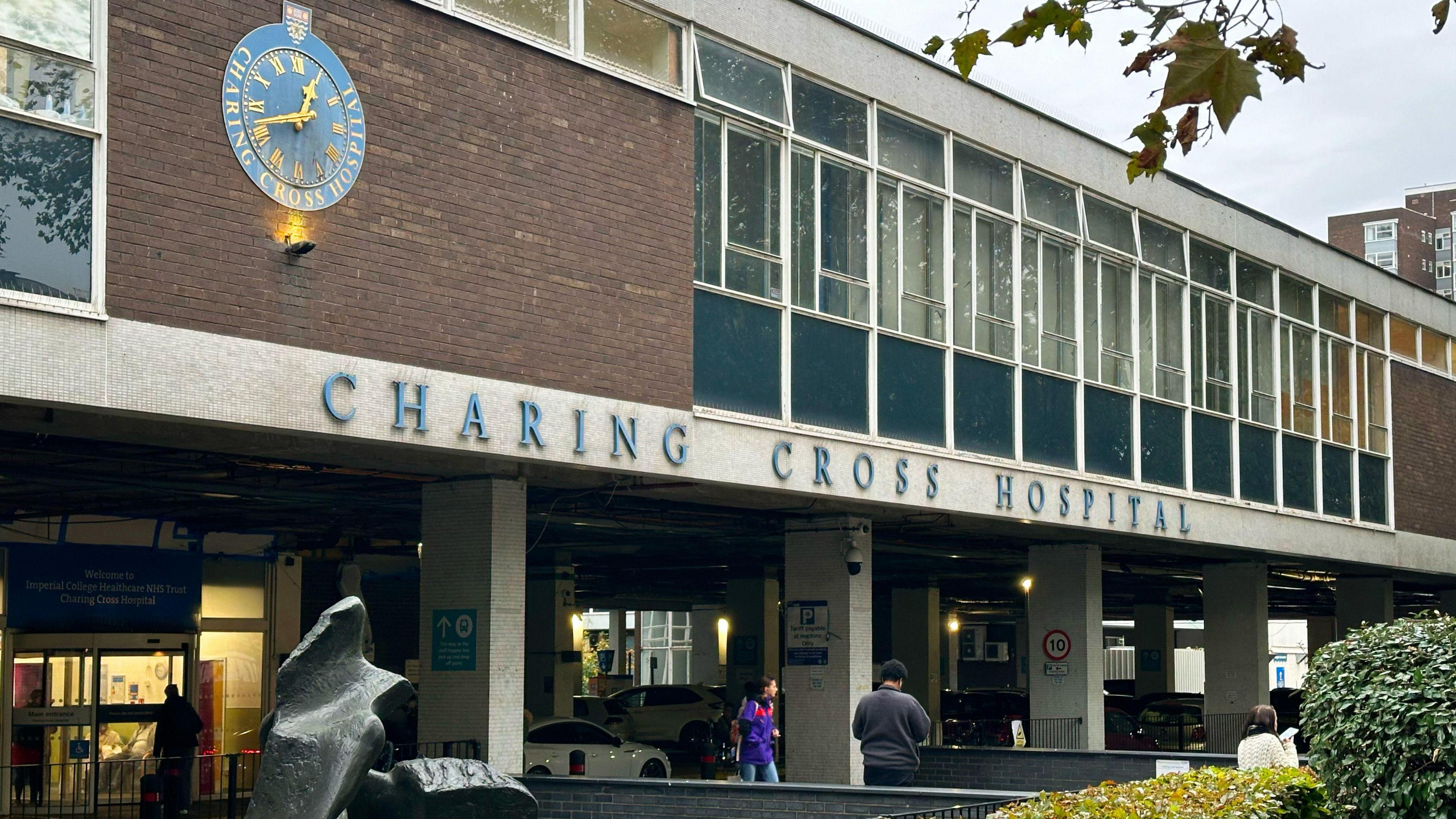 Charing Cross Hospital exterior shows blue signage, clock and patients beneath blue-clad windows