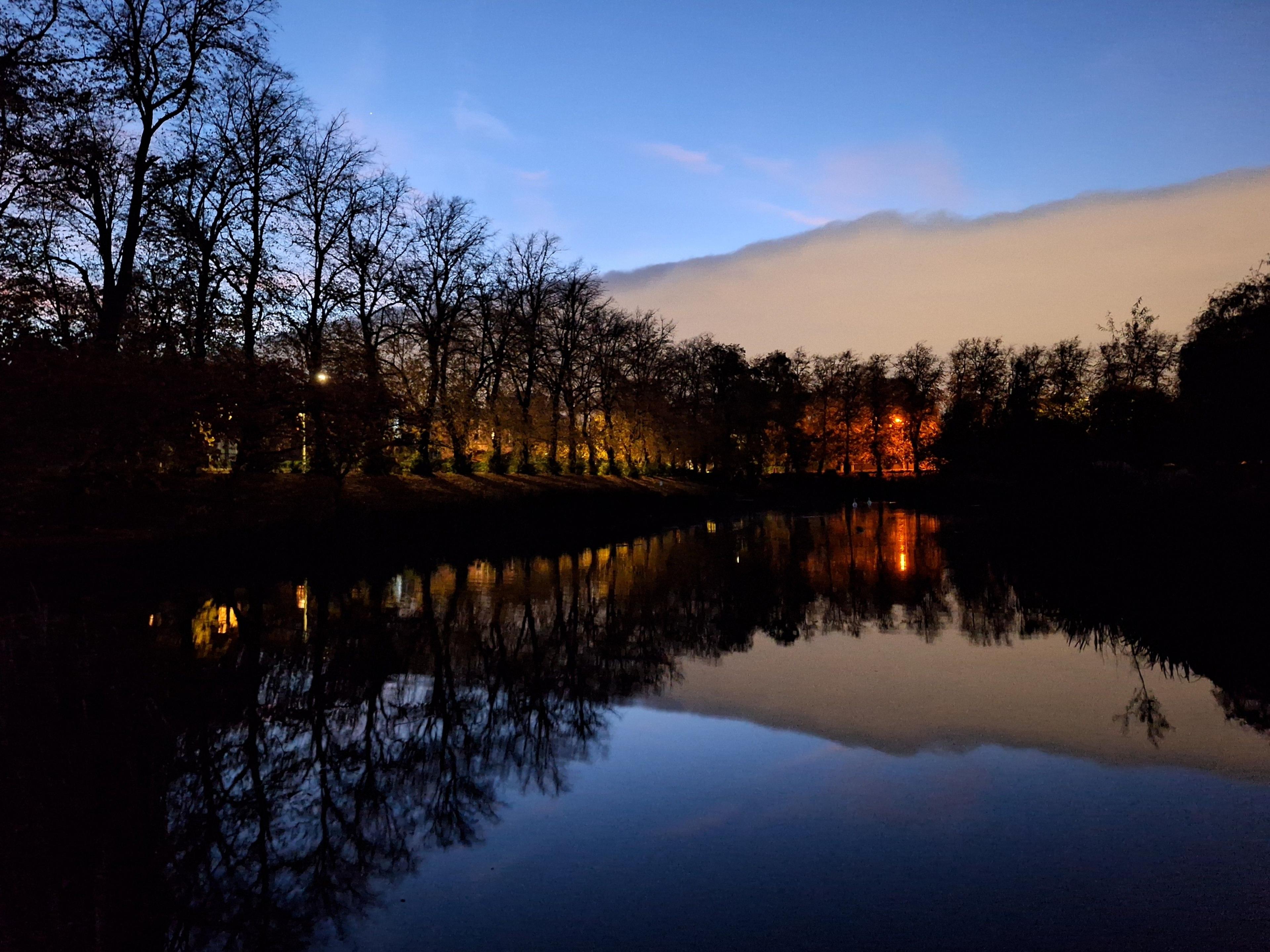 A pond, lined by trees, with a dense bank of clouds above it - the clouds are so dense they resemble a mountain