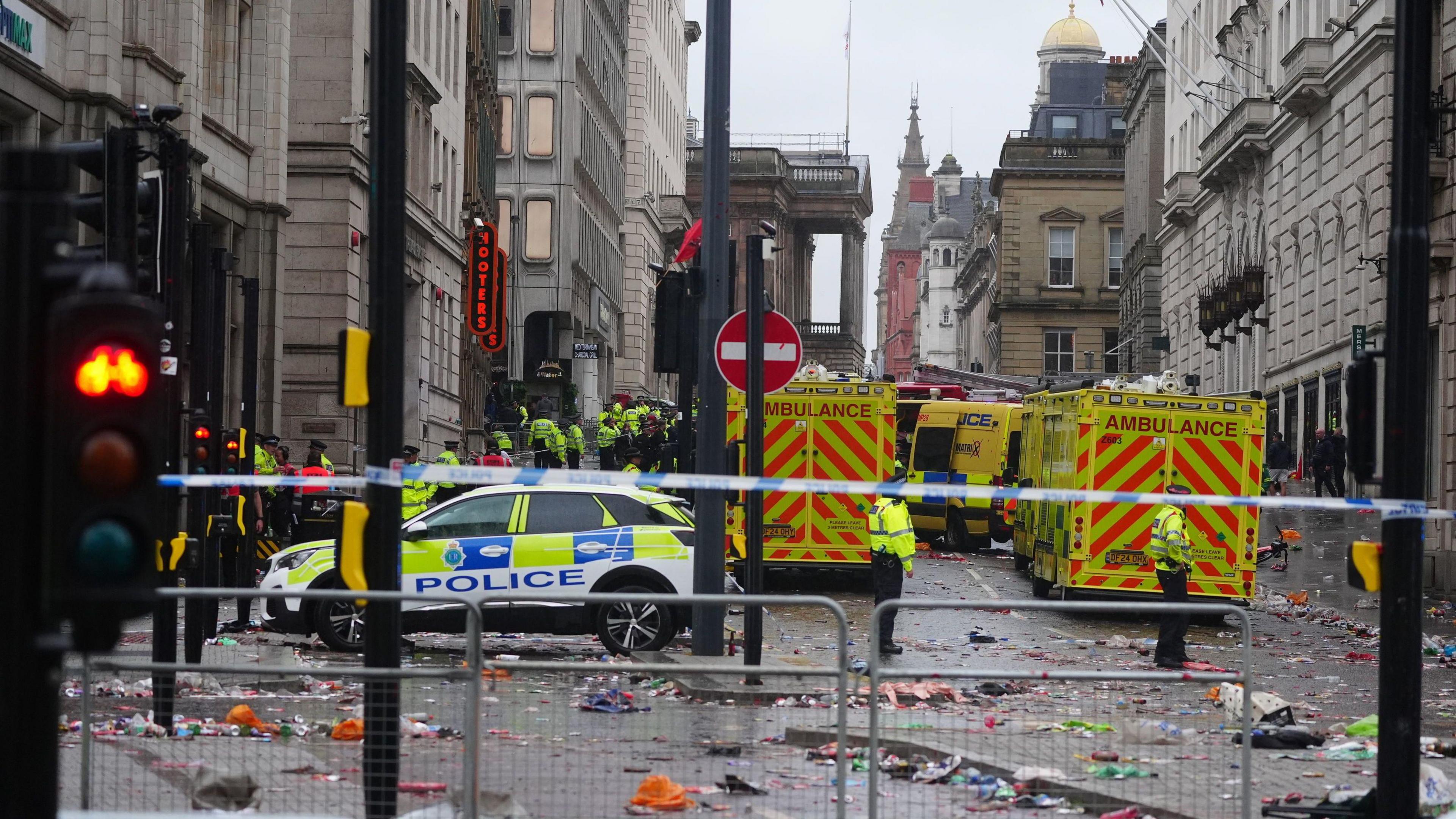 Police and emergency personnel dealing with an incident near the Liver Building in Liverpool during the Premier League winners' parade. There are at least three ambulances and a police car lying behind police tape. There is much detritus lying on the road.