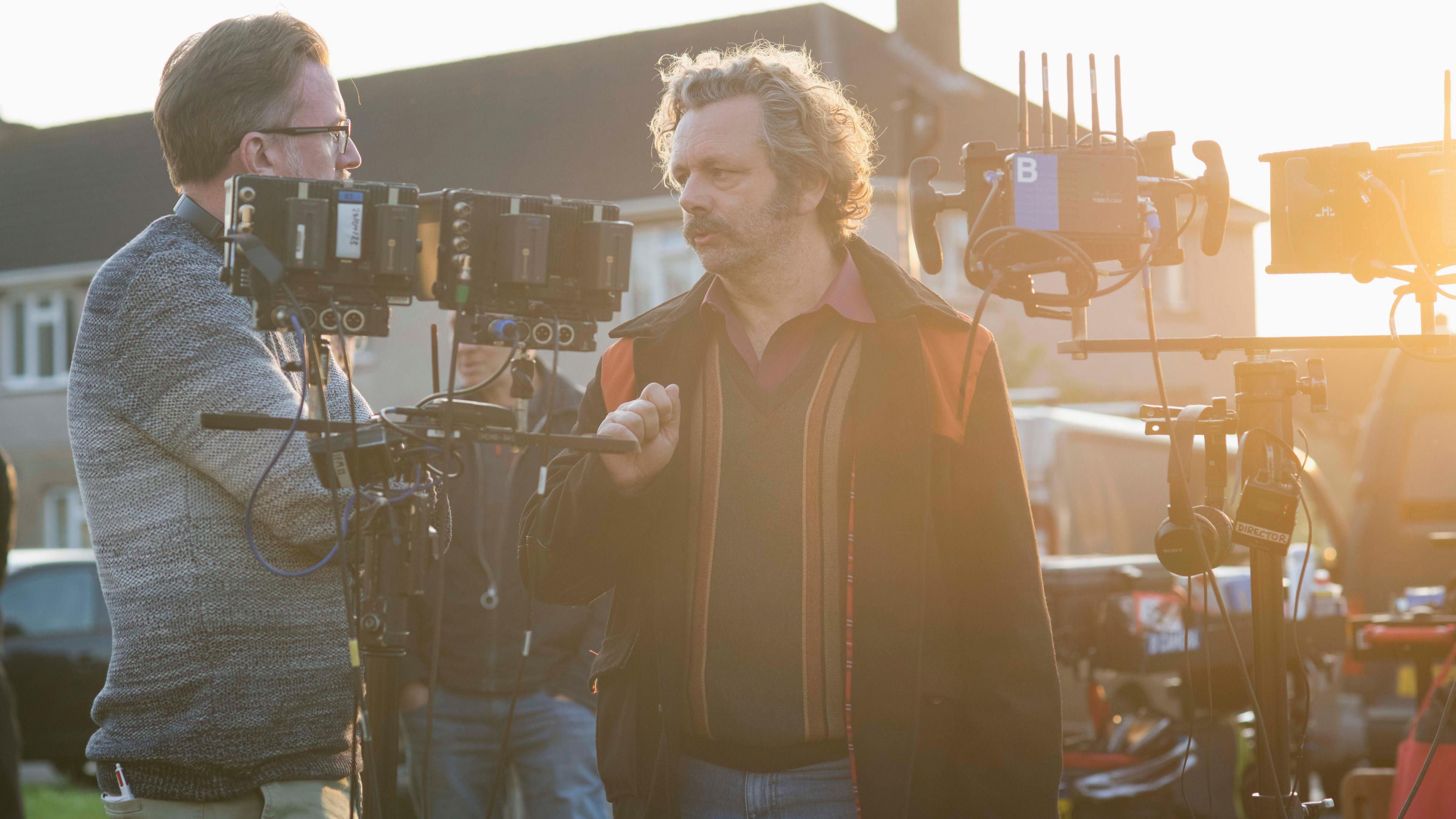 Yr actor Michael Sheen yn siarad gyda dyn ar set ffilm