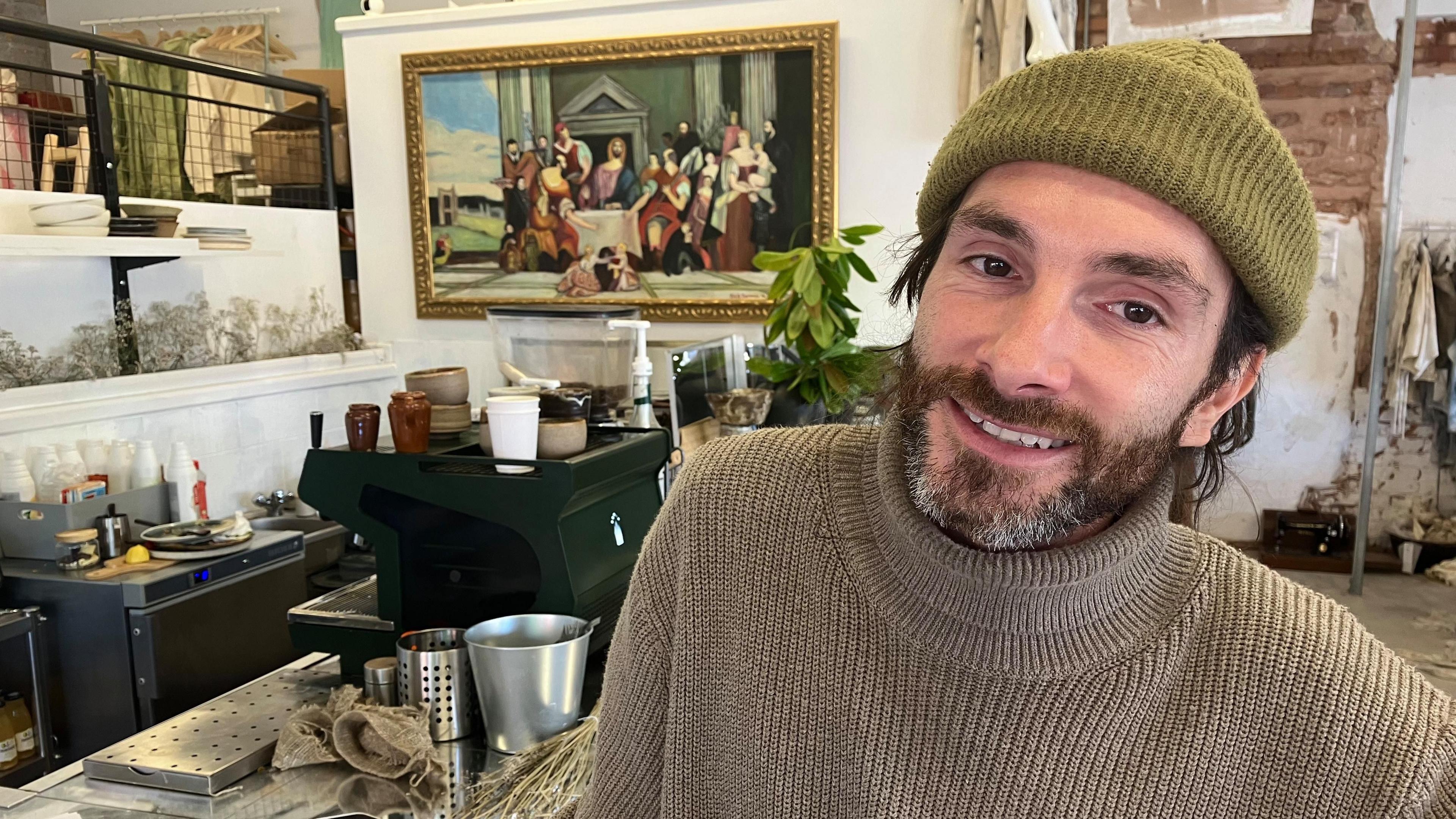 a man in a hat in front of a painting in a cafe