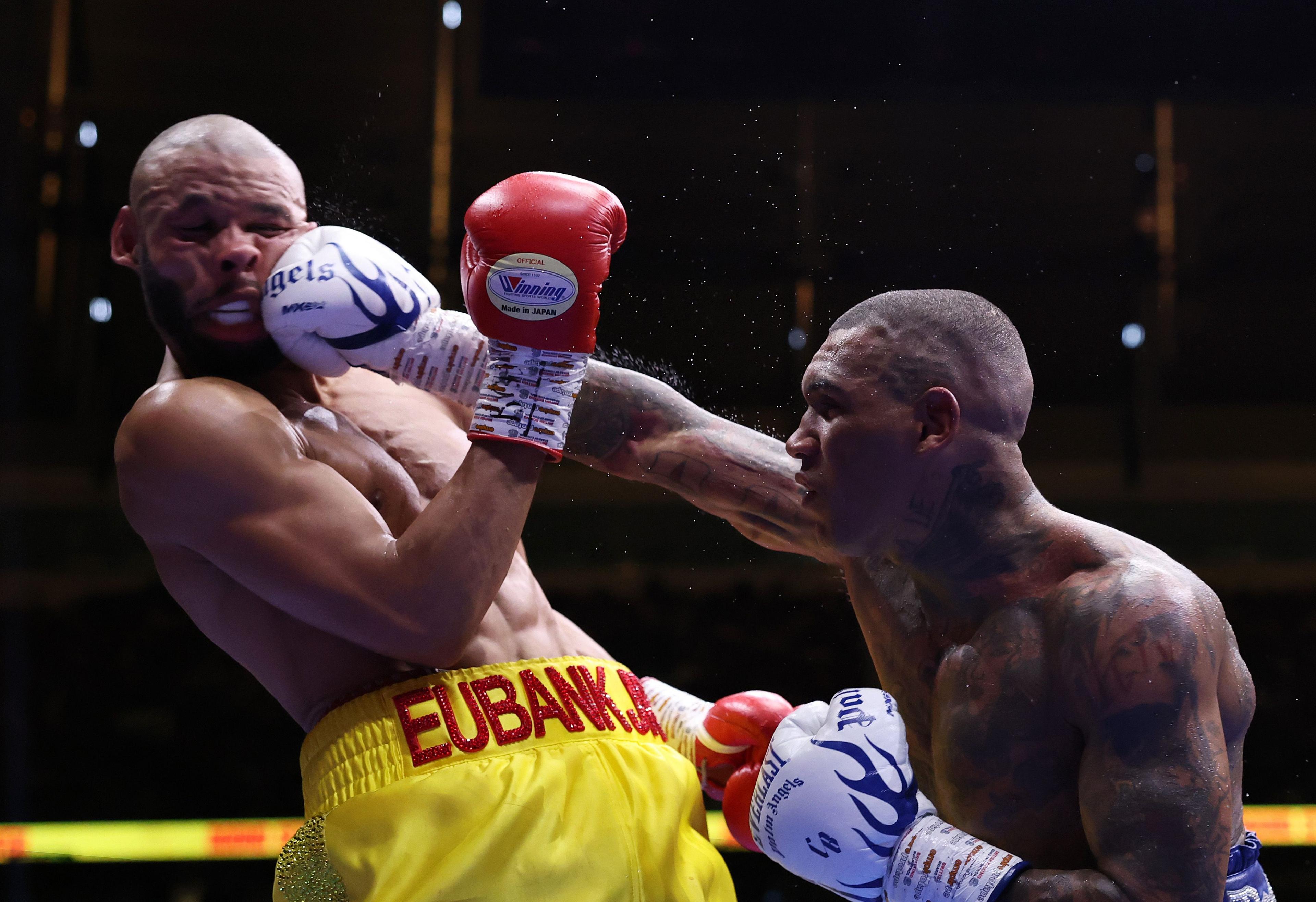 Two boxers in a ring during a match, one delivering a powerful punch to the other’s face. The boxer being hit is wearing yellow trunks with “EUBANK” written on the waistband.