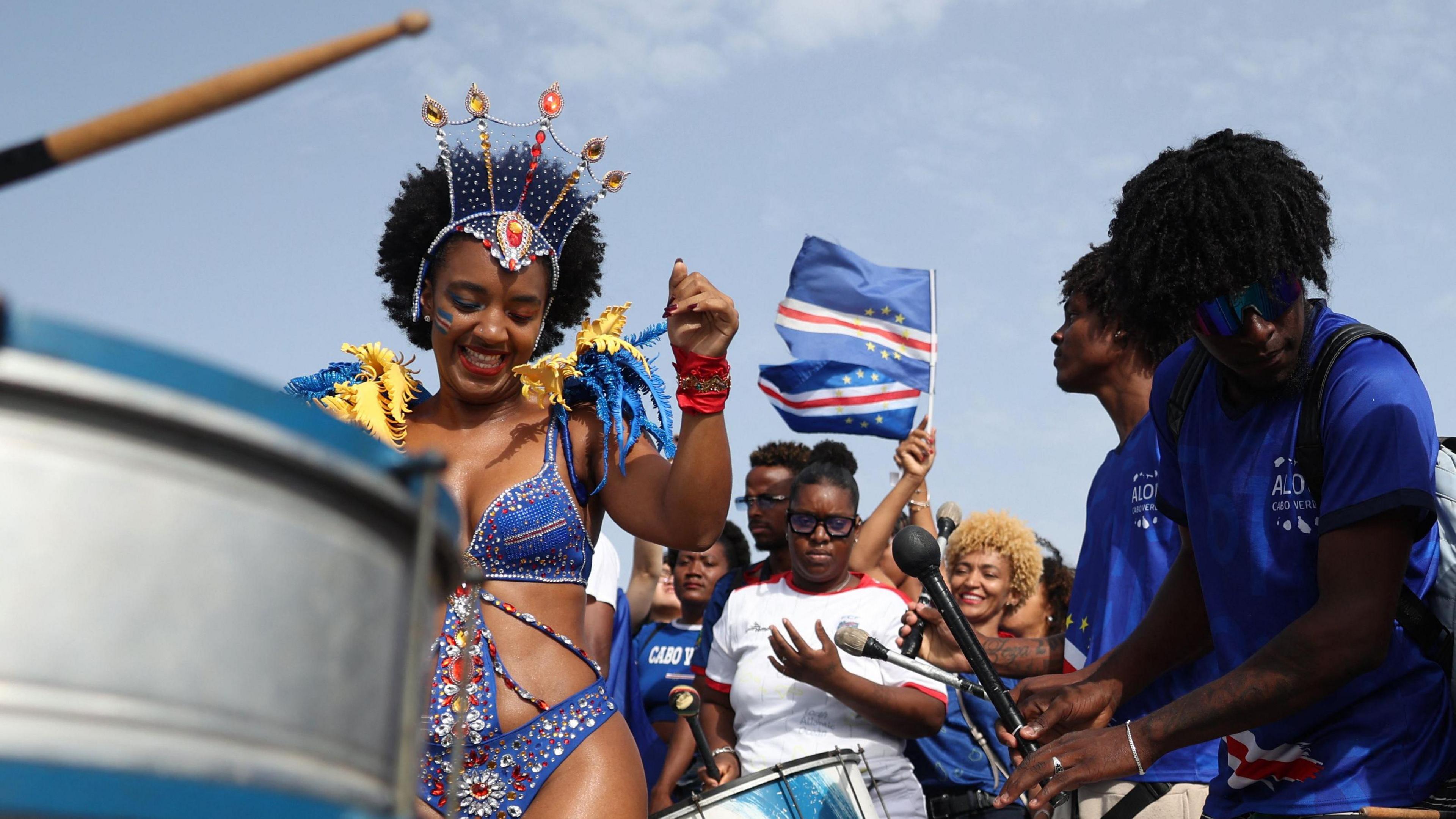 A lady in a blue, red and white carnival outfit dances amongst a crowd