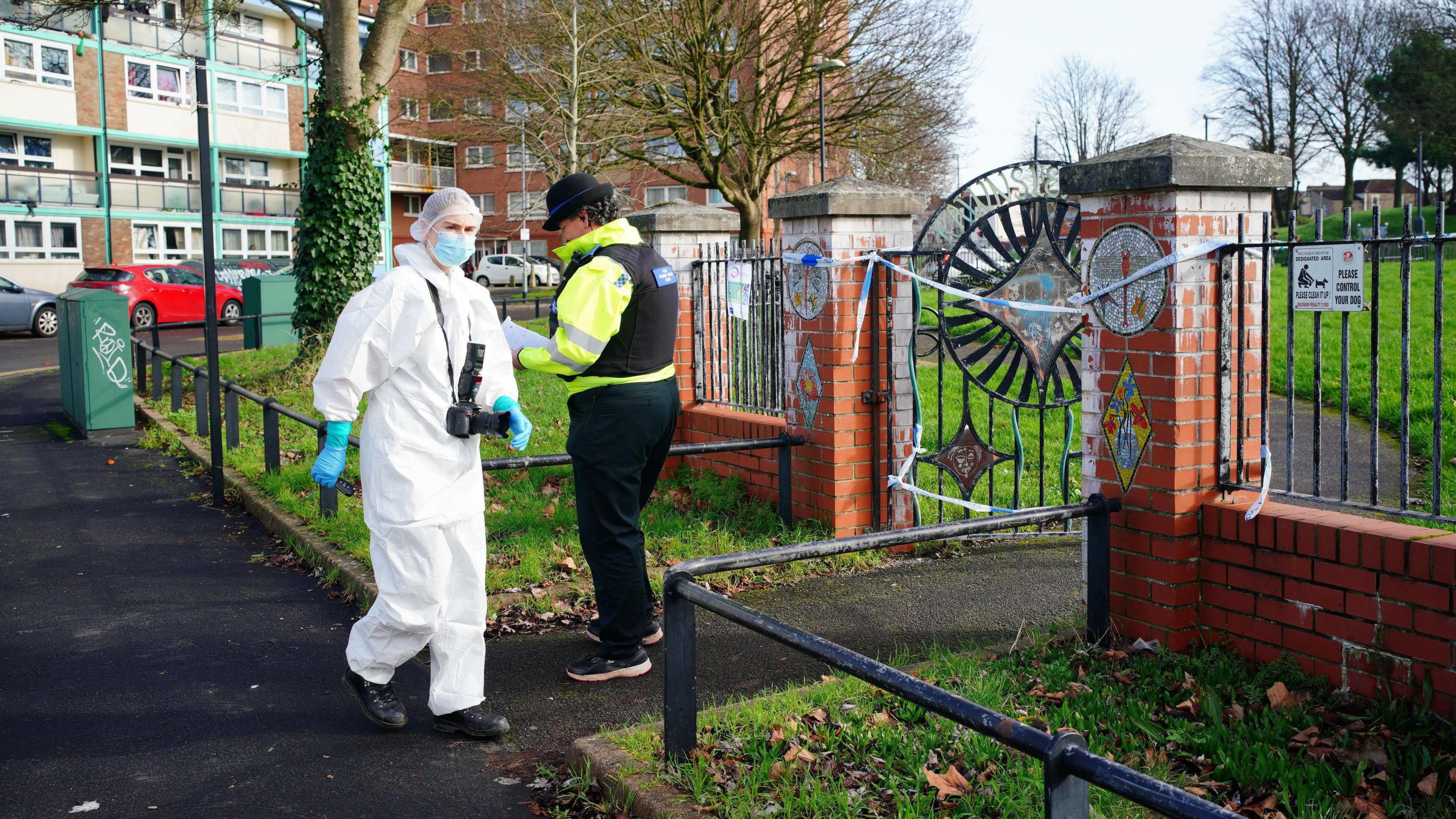 A police officer and a member of the forensic team in PPE outside Rawnsley Park. The entrance is cordoned off.