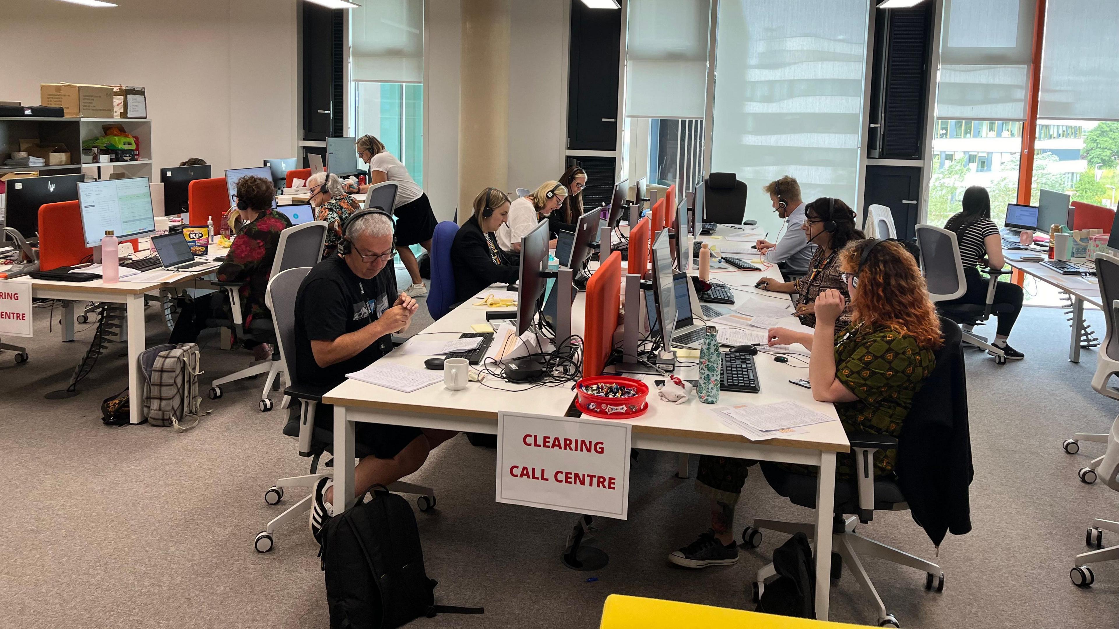 Lots of people with headsets sit round a table answering phones for students with clearing questions 