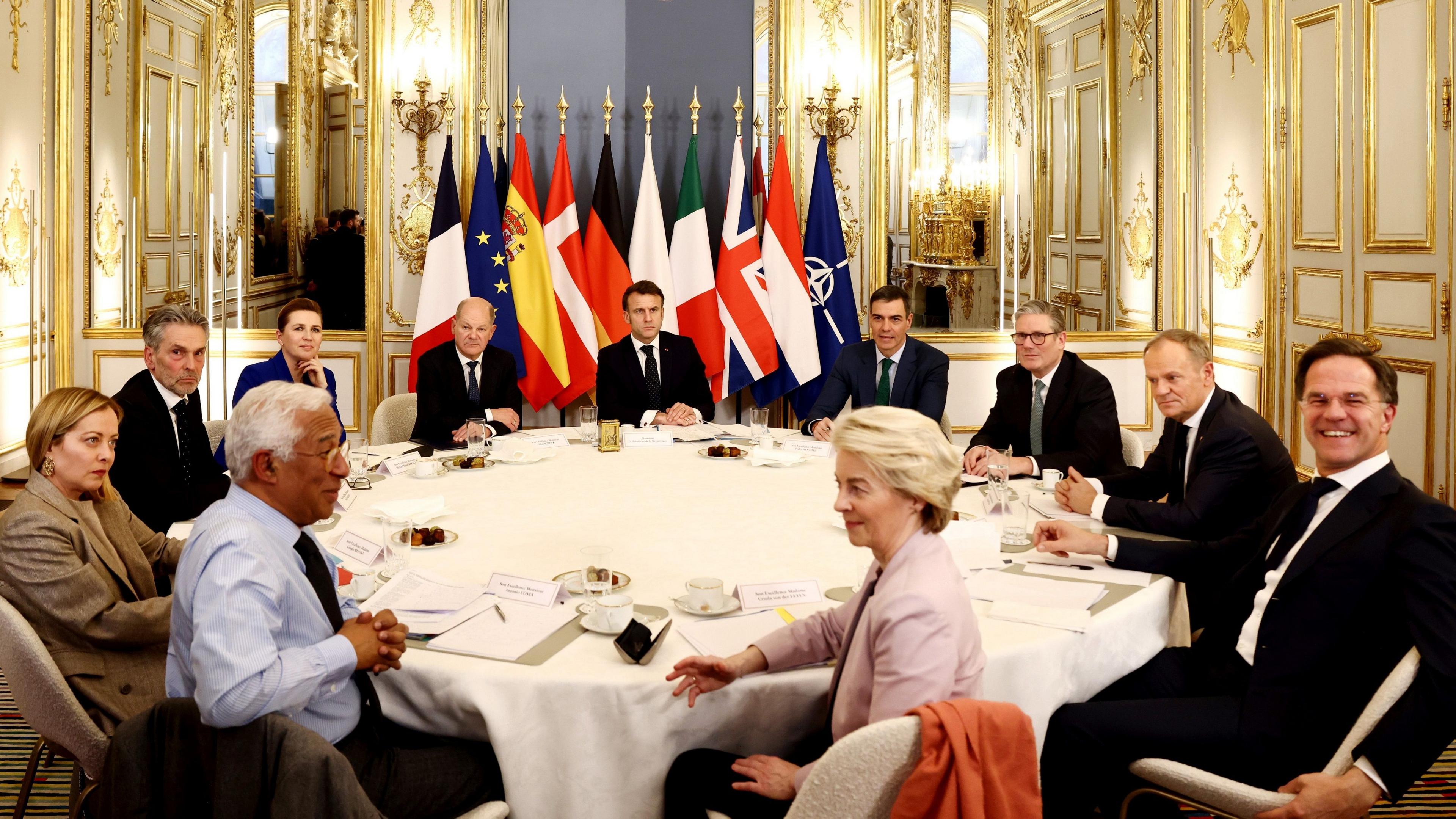 European leaders sit around a table in the Elysee Palace with flags in a line behind them. In the middle sits European Council President Antonio Costa and European Commission President Ursula von der Leyen, and from left to right: Italian PM Giorgia Meloni, Dutch PM Dick Schoof, Danish PM Mette Frederiksen, German Chancellor Olaf Scholz, French President Emmanuel Macron, Spanish PM Pedro Sanchez, UK PM Keir Starmer, Polish PM Donald Tusk, and Nato secretary general Mark Rutte.