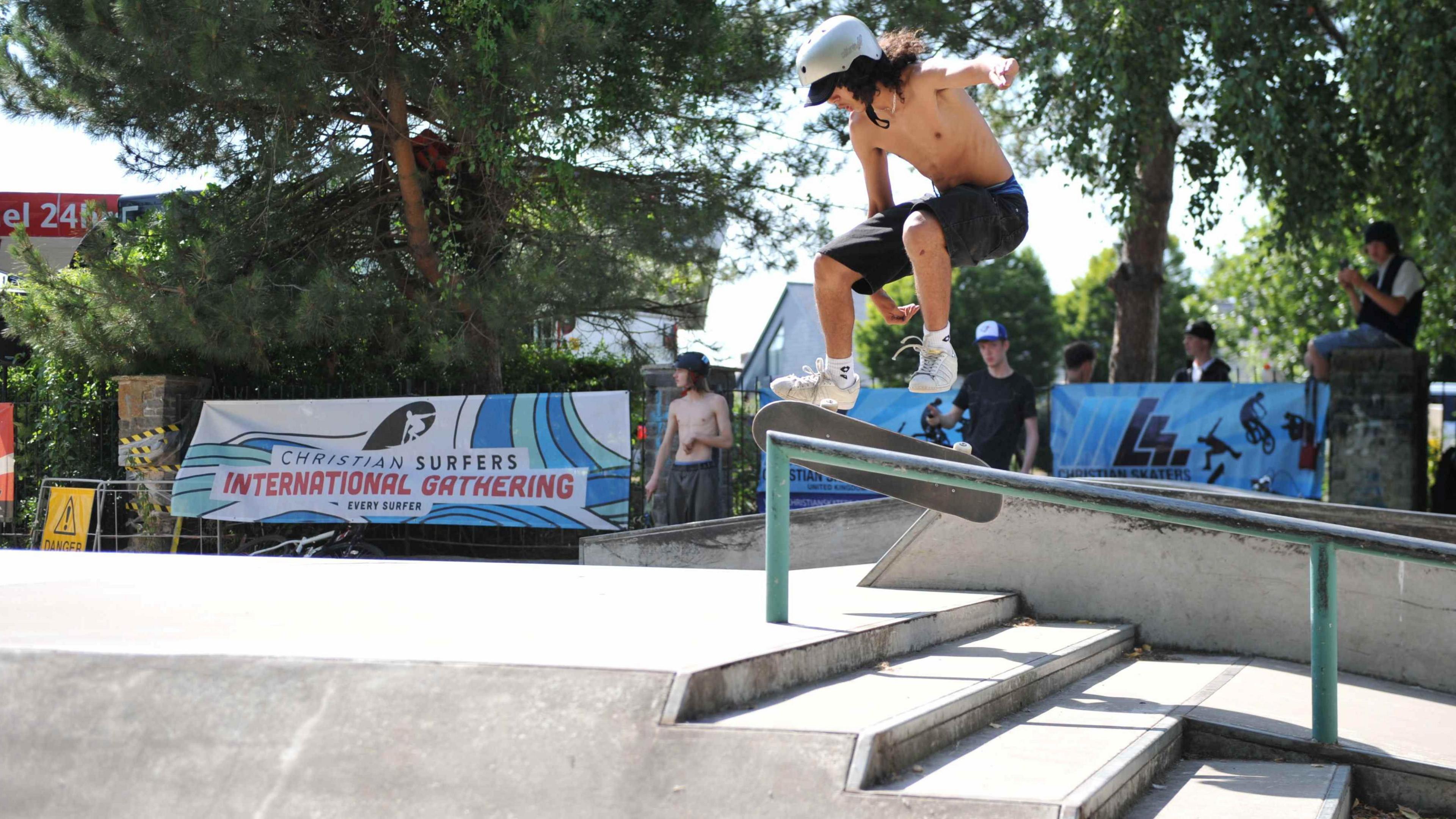 A skateboarder without a top on performing a jump on a railing