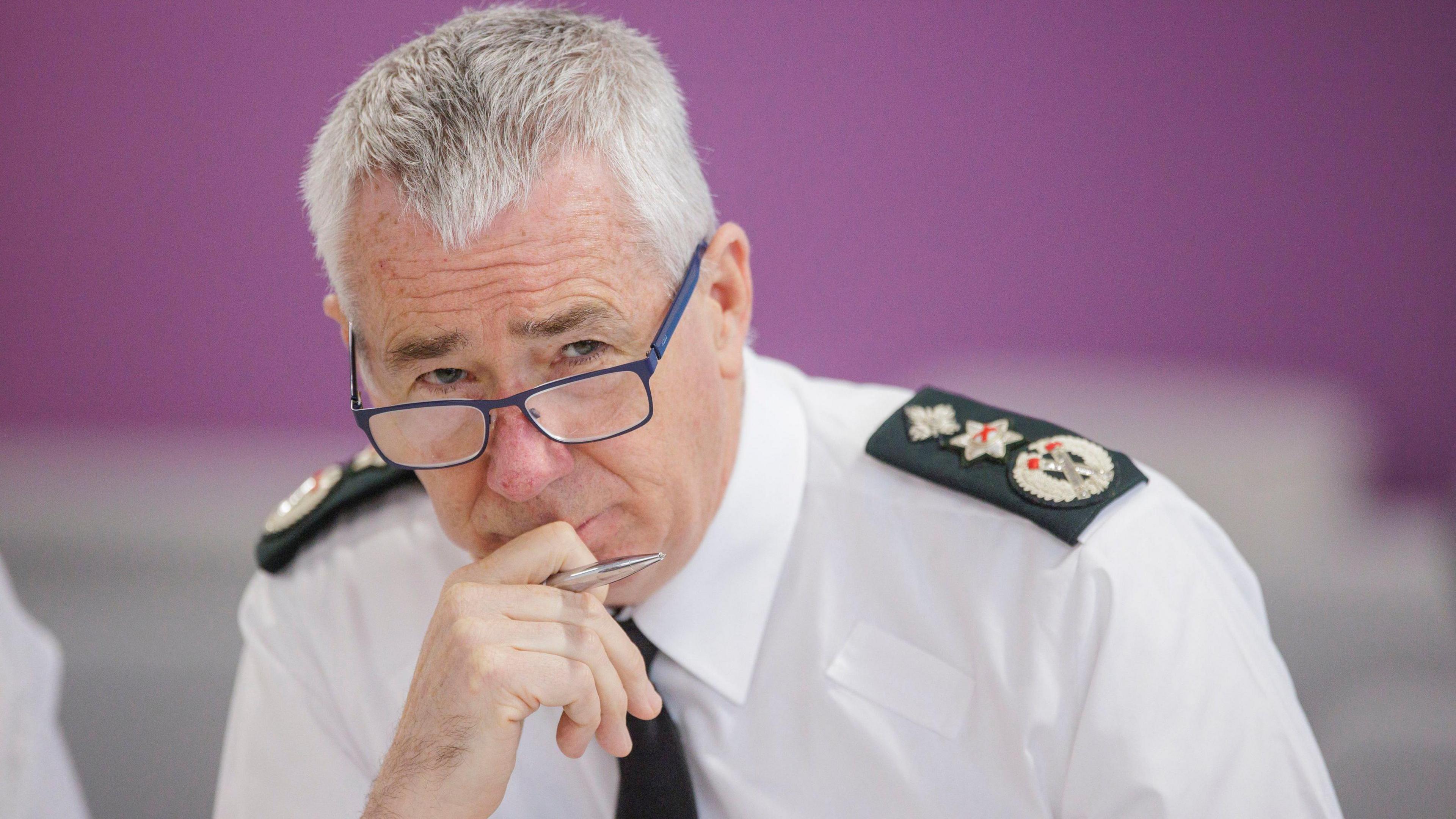 Chief constable Jon Boutcher holds his hand to his chin- in  his hand is a silver pen. He is wearing police uniform