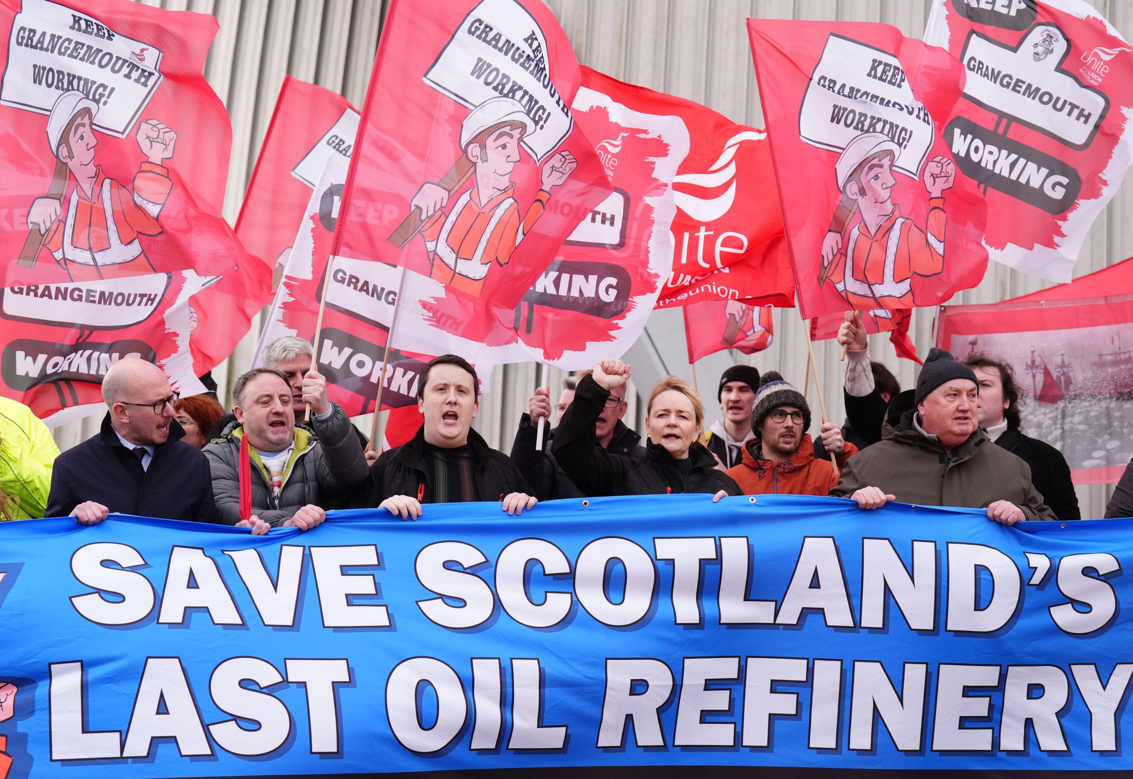 Unite General Secretary Sharon Graham at the centre of a line of workers shouting in protest outside the oil refinery. They all hold up large union flags at the demonstration in February 2025