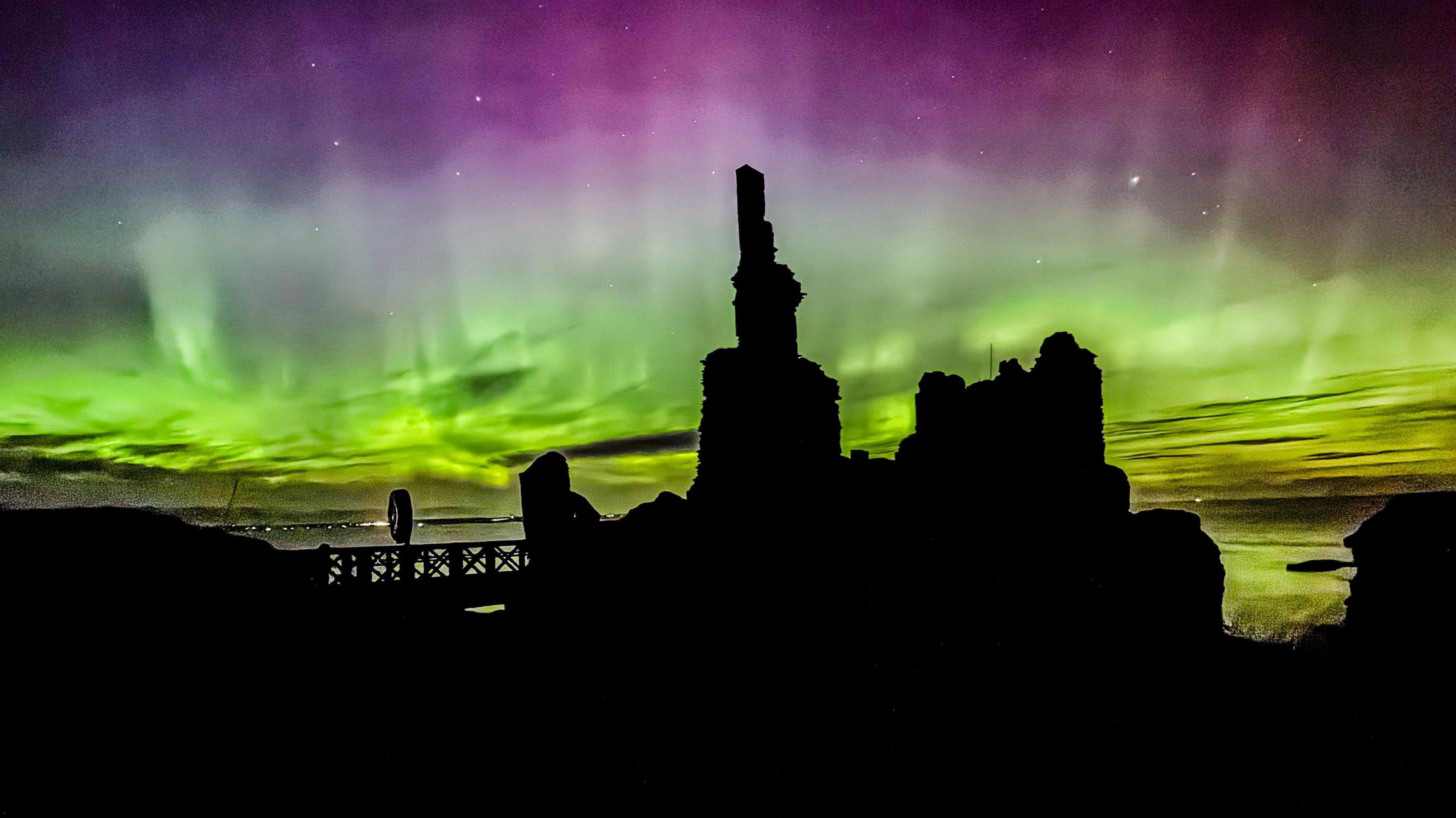 A breathtaking scene featuring the Aurora Borealis - vivid green and purple hues dance across the night sky while a dark castle building stands in stark contrast to the luminous sky, adding depth and mystery.