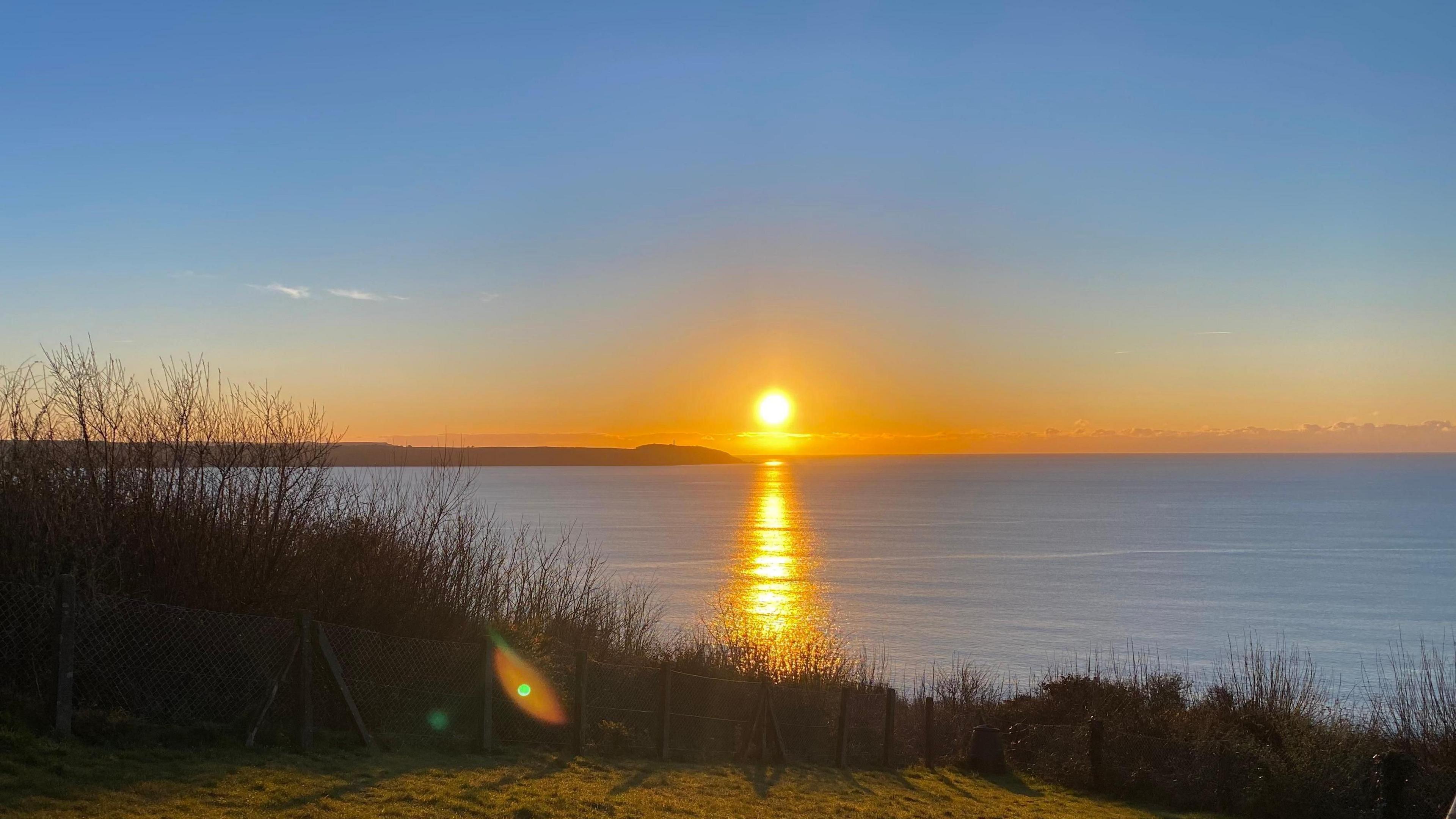 looking out to sea with a bright yellow sunrise coming above the horizon