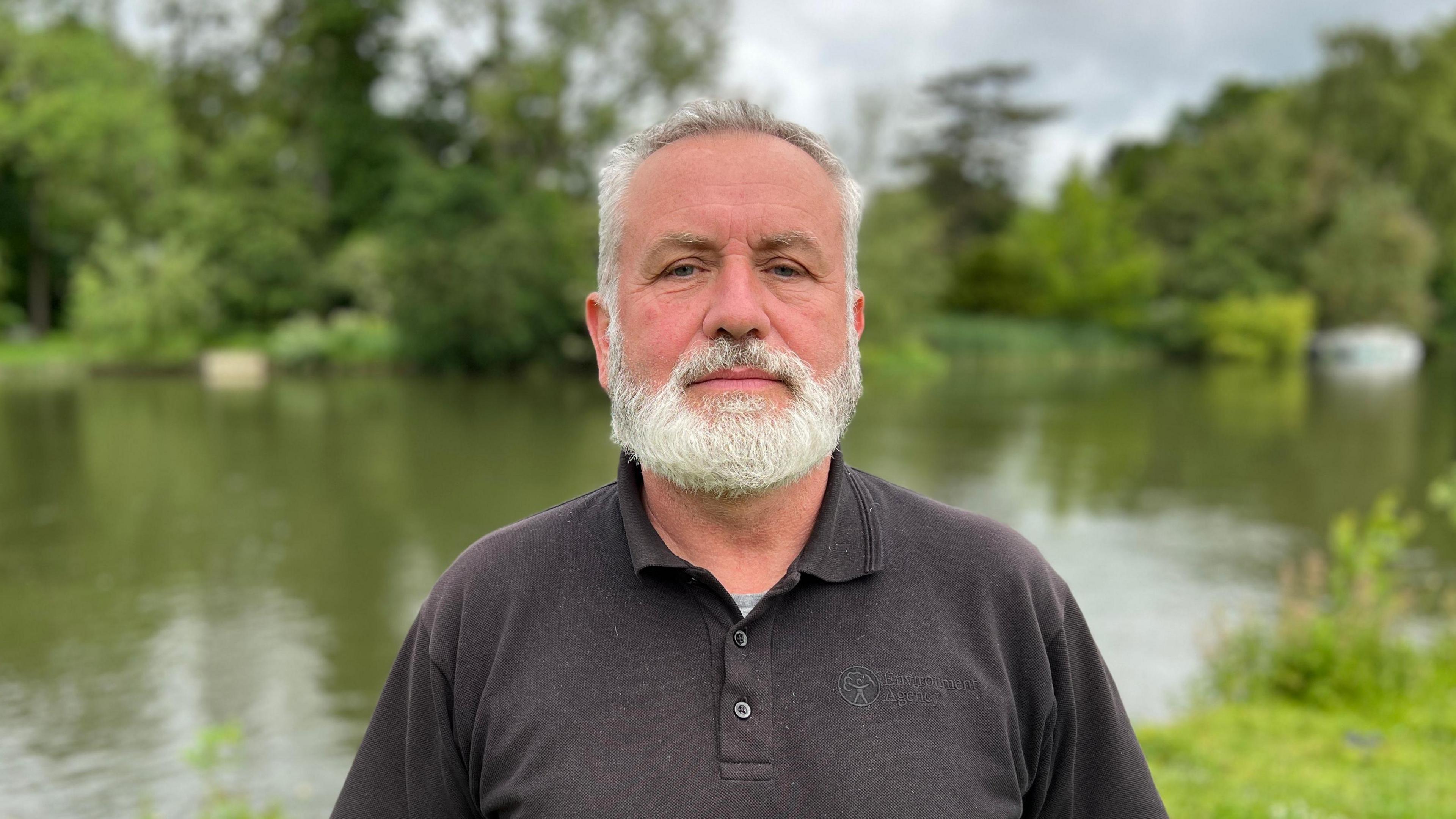 Russell Robson has white, short hair and a white beard, and is wearing a black, buttoned-up Environment Agency T-shirt