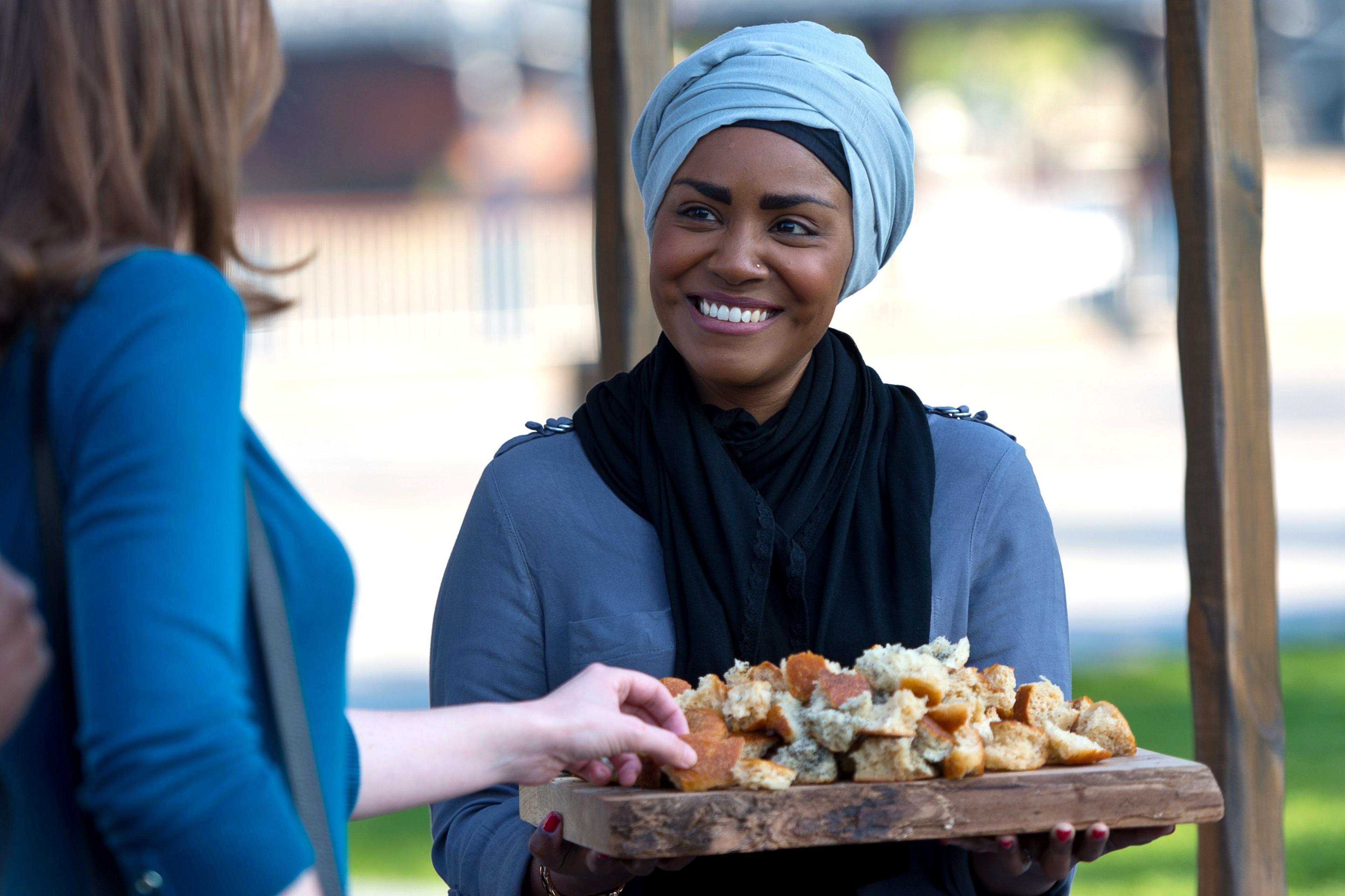 nadiya hussain holding a tray of bread sample alongside a woman taking one of the samples