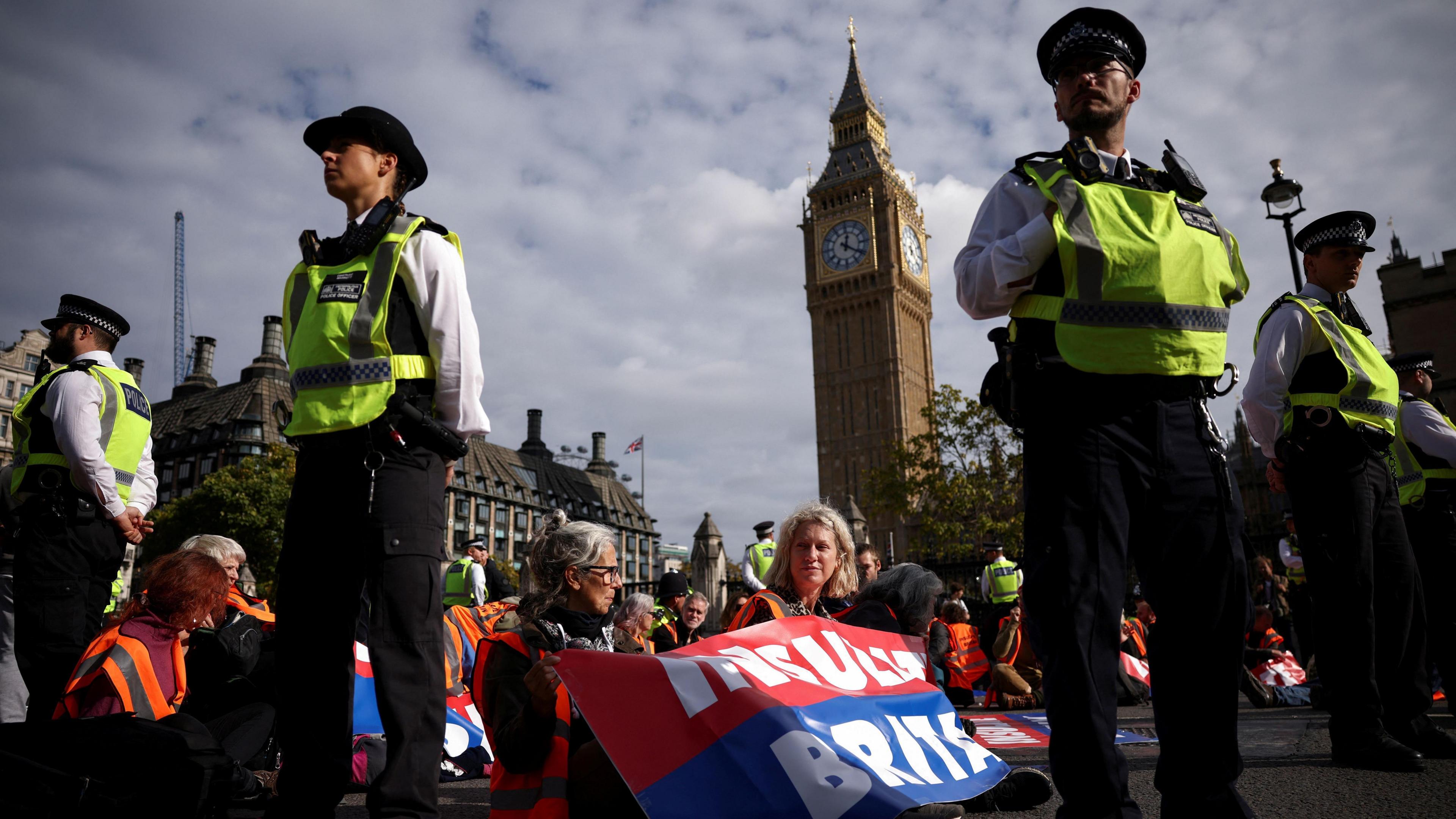Police officers standing around Insulate Britain activists who are blocking a road outside the Houses of Parliament in a sit-down protest