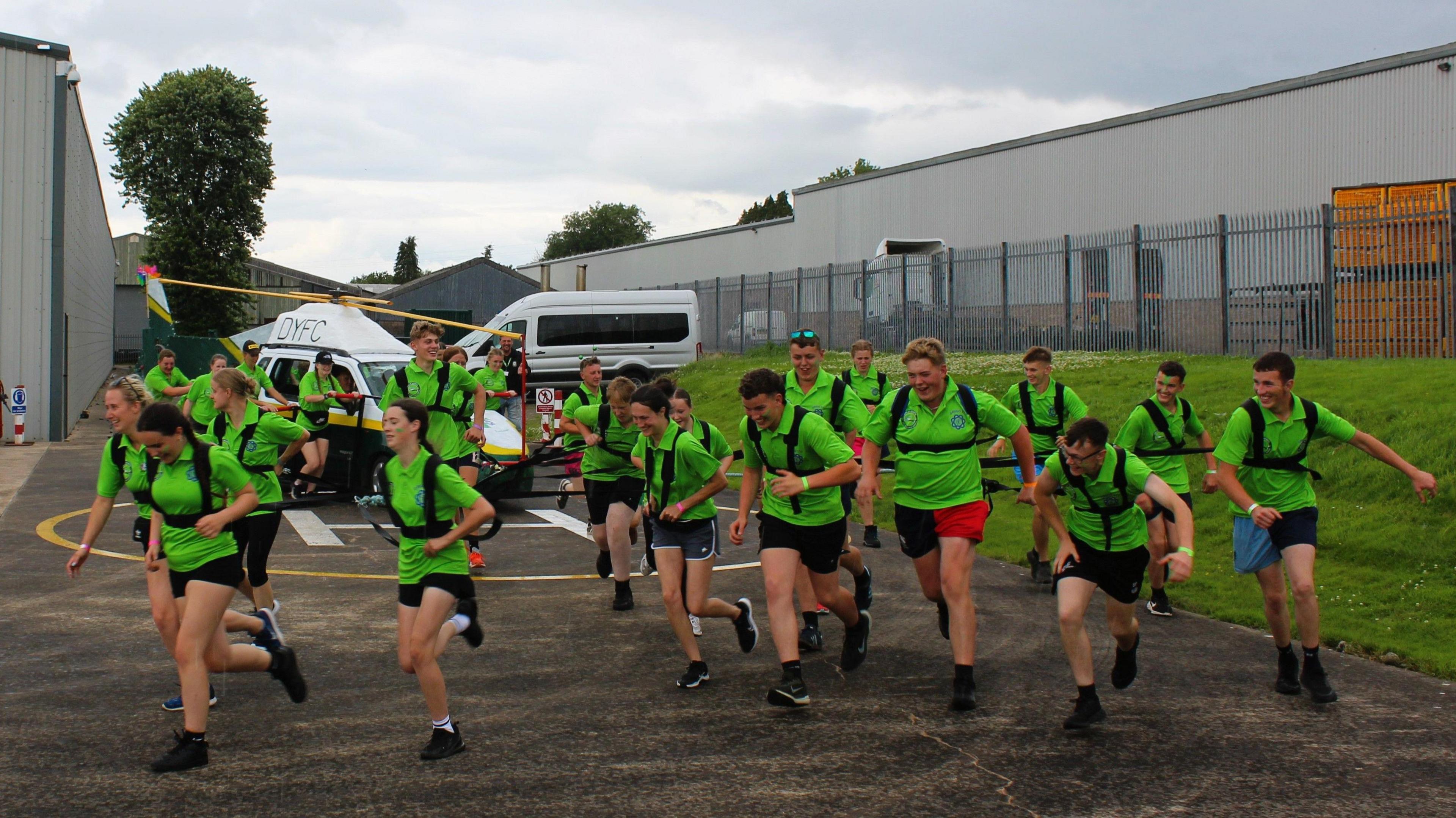 More than a dozen young farmers, wearing bright green t-shirts, pull the replica helicopter onto the air base. They are running with smiles on their faces.