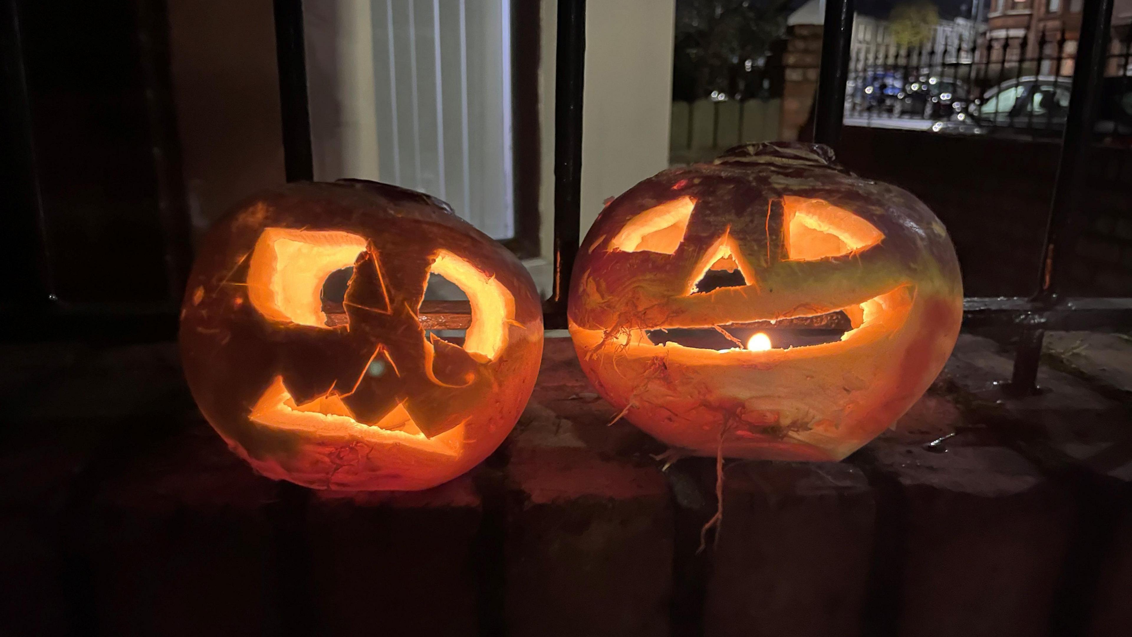 Two carved pumpkins sit on a wall. It's night time and the candles inside illuminate them.