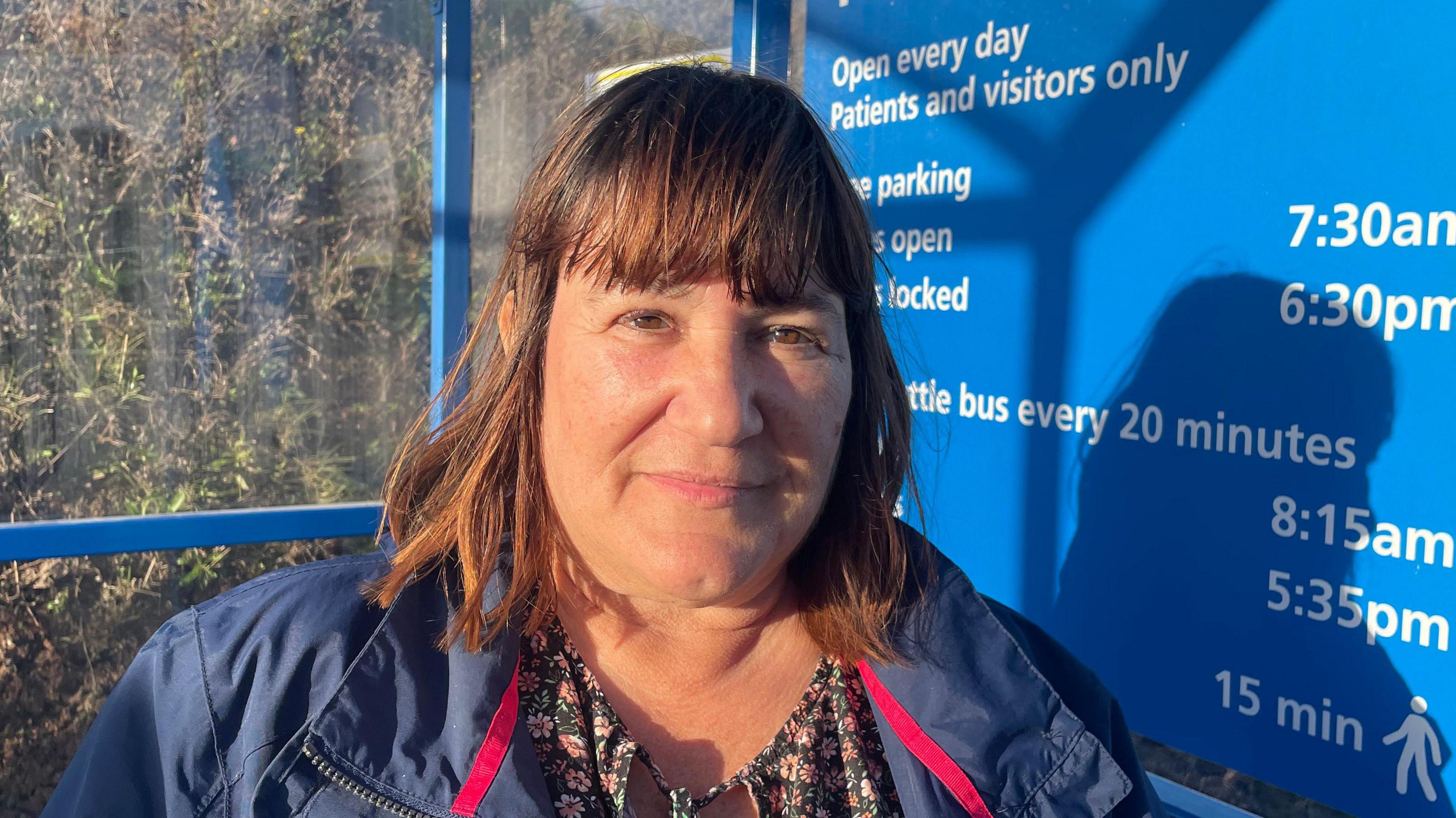 Woman with shoulder length brown hair in a floral top and blue jacket