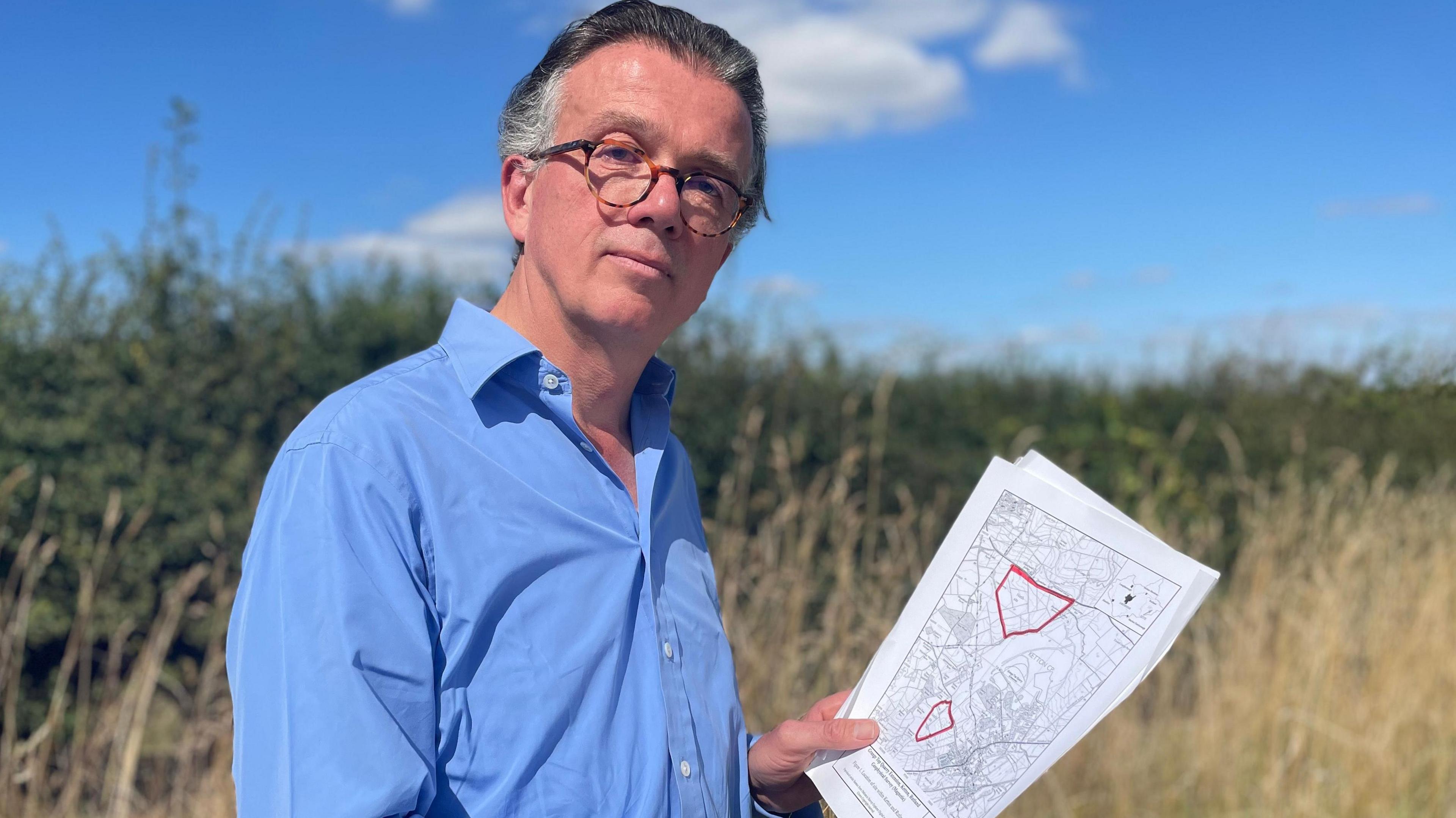 Campaigner Matthew Eatough standing in a field holding quarry plans.