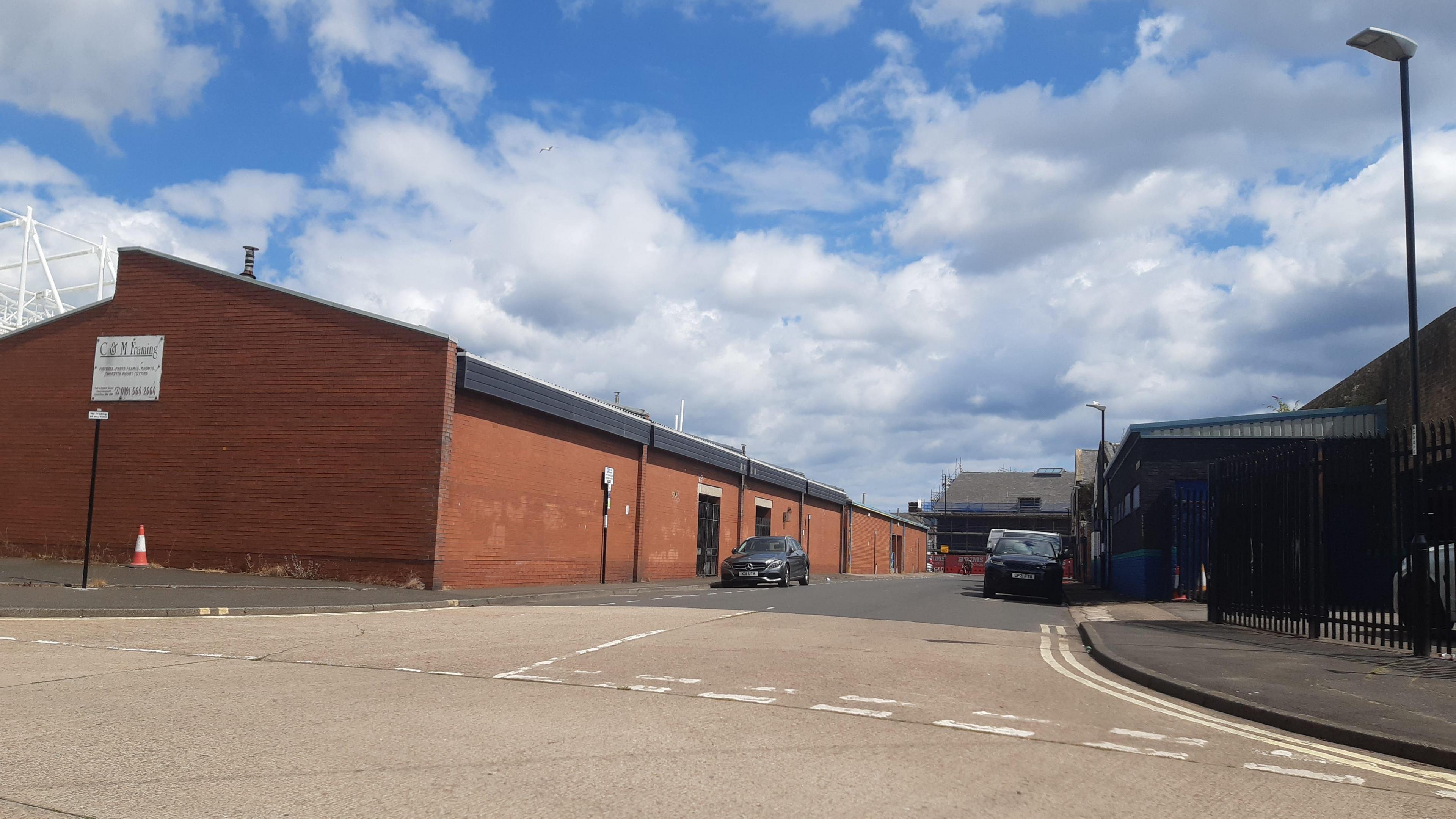 Brown buildings on deserted road, save for two parked cars, on an industrial estate.