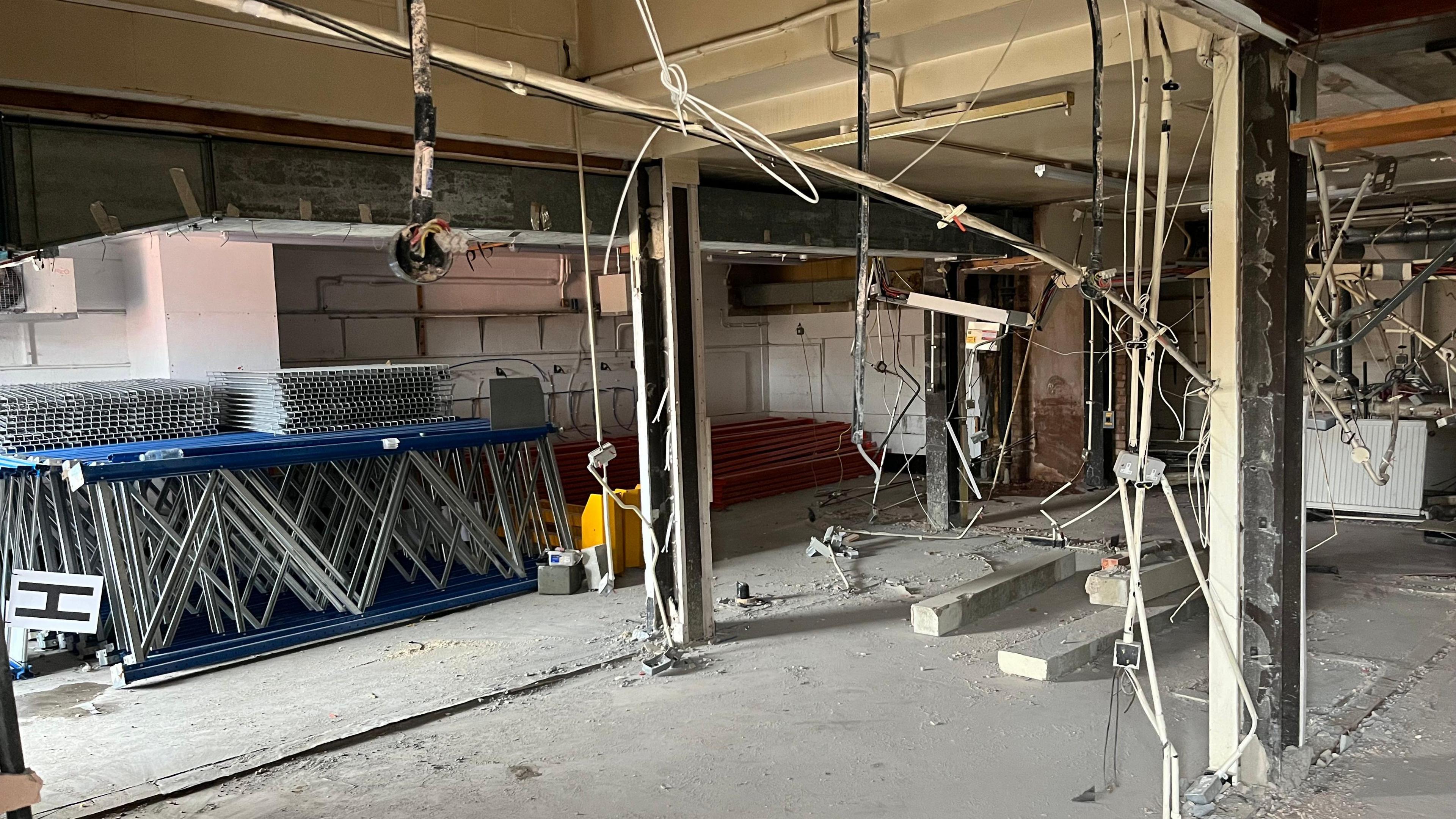 The inside of a former pub with flooring, ceiling and walls removed, lots of electrical wires hanging from what looks like steel supports vertical and horizontal.