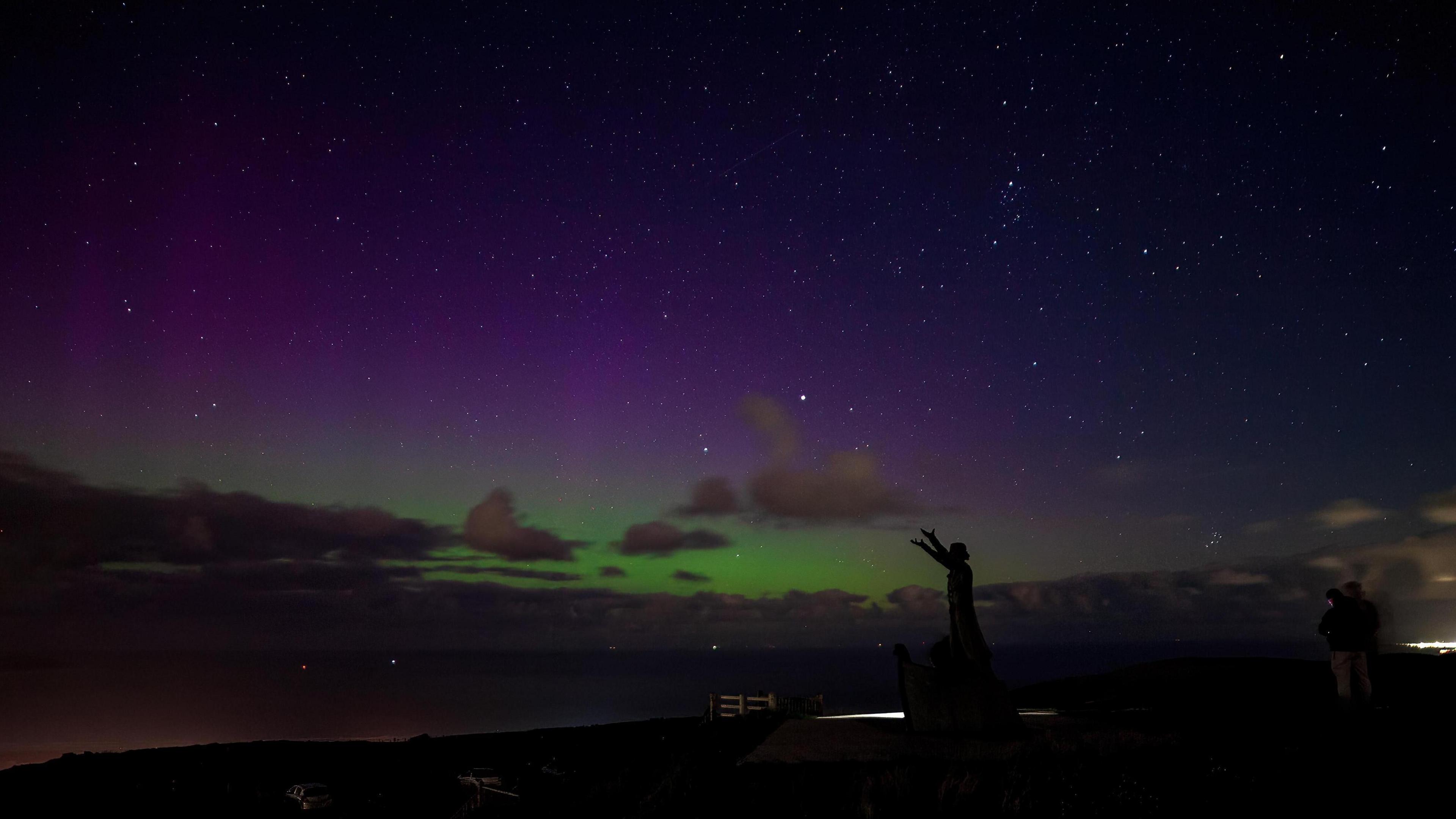 A women's silhouette is seen in the foreground with the Northern lights in the background