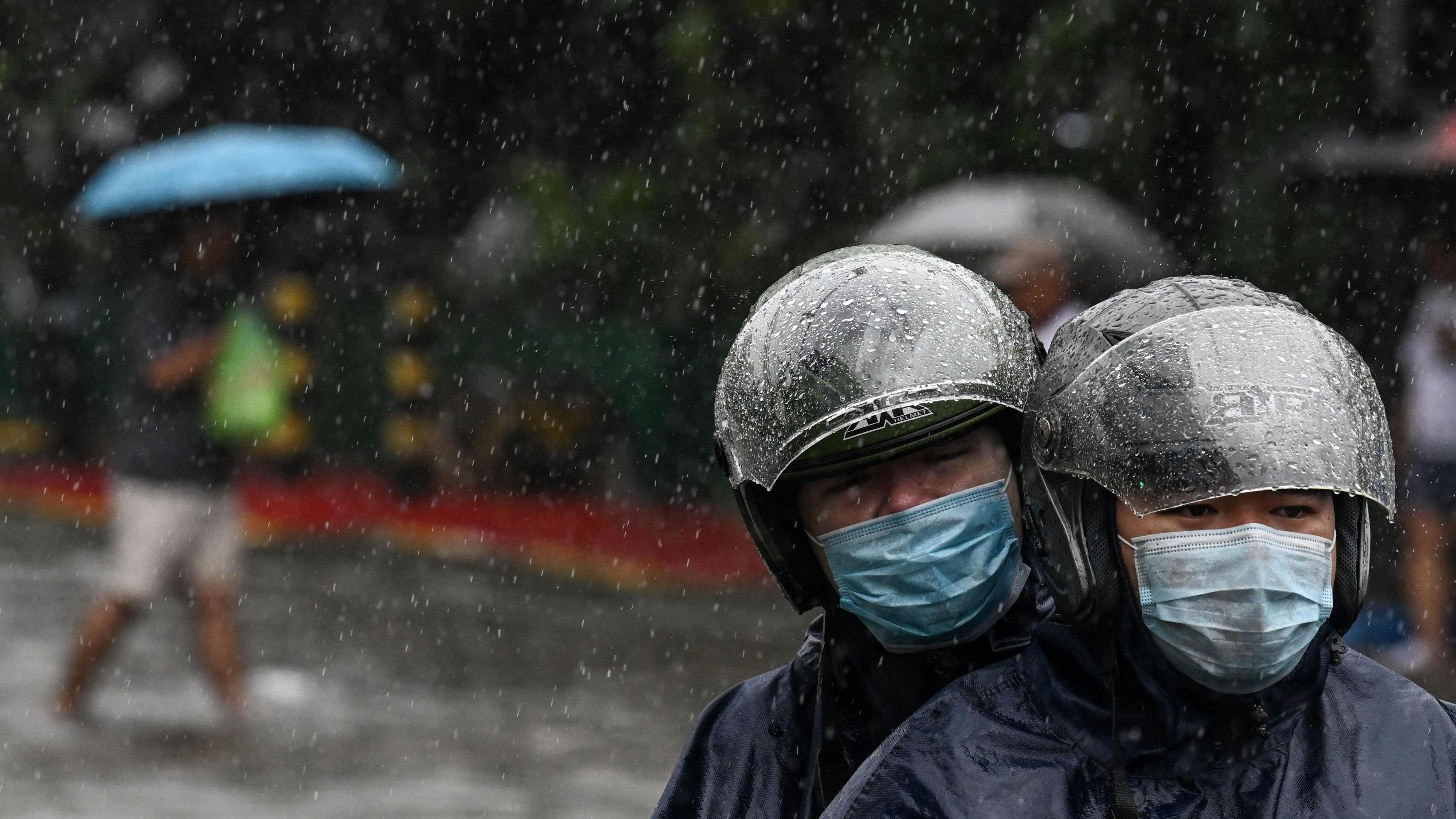 A couple wearing helmets riding a motrbike under the rain