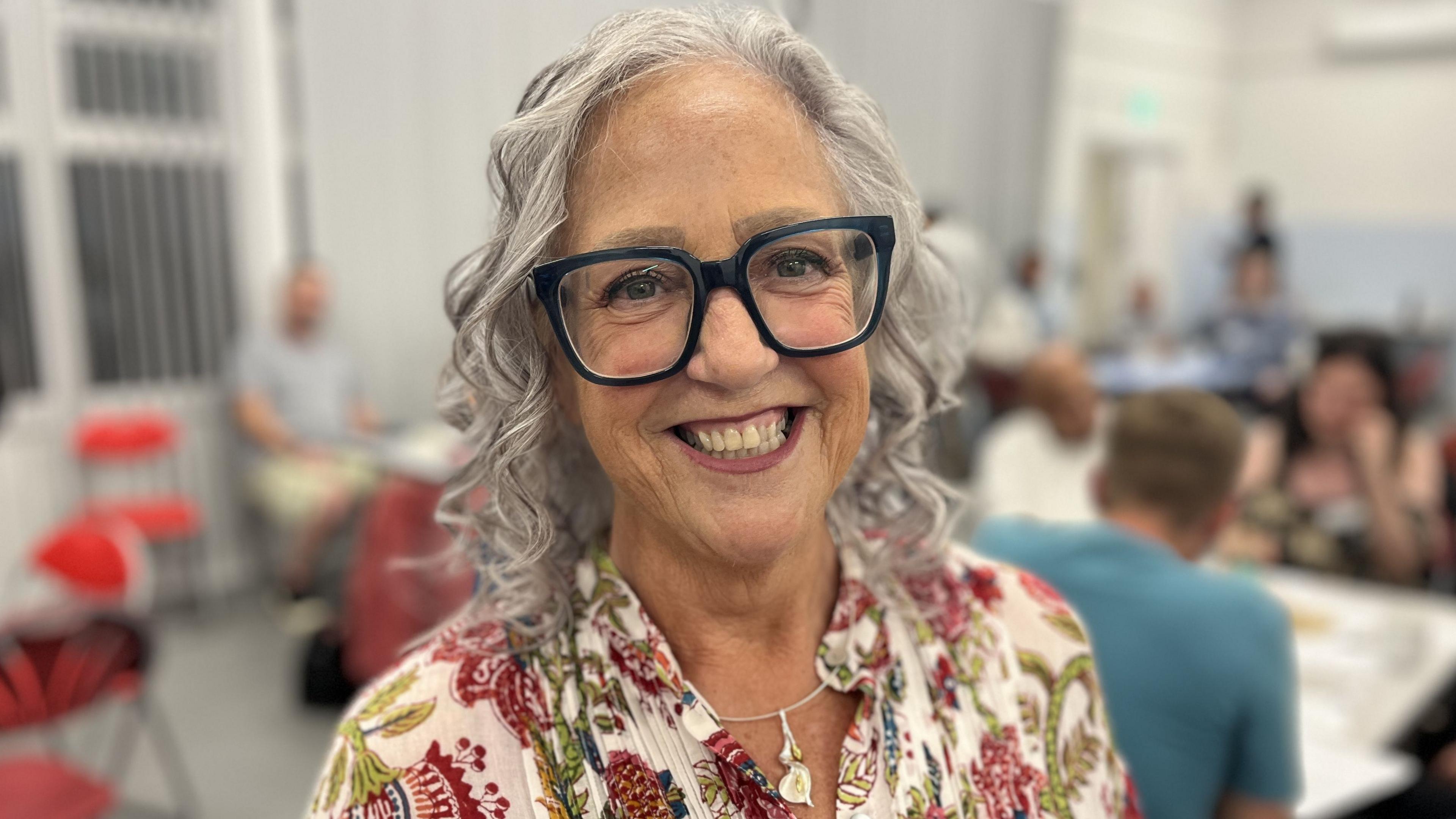 Primary School Teacher, Debbie Brown, wearing large black framed glasses with curly shoulder length grey hair