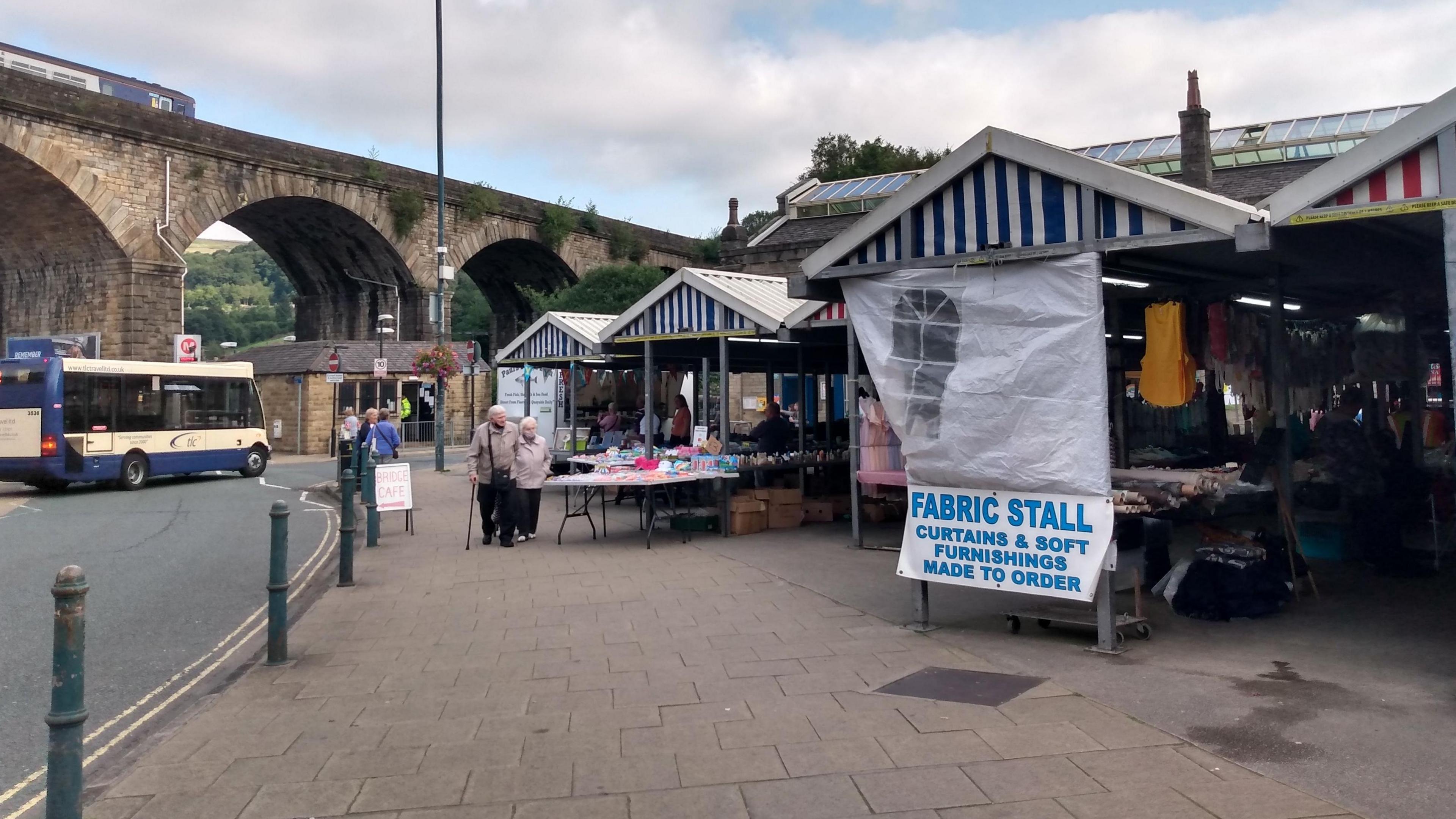 A railway bridge in the distance with a road beneath it and to the right of the picture a number of market stalls