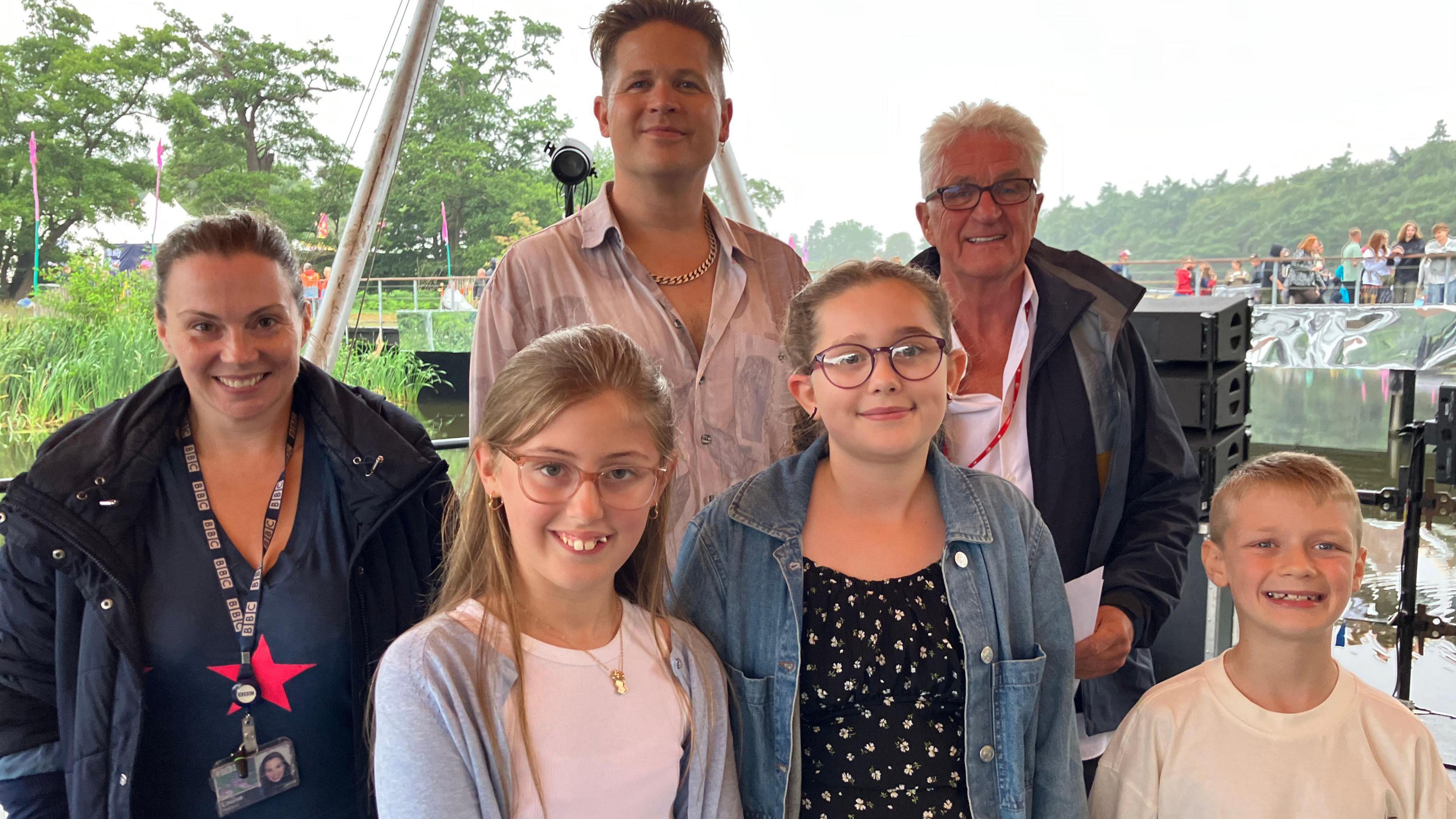 Three adults and three children stand on a festival stage.