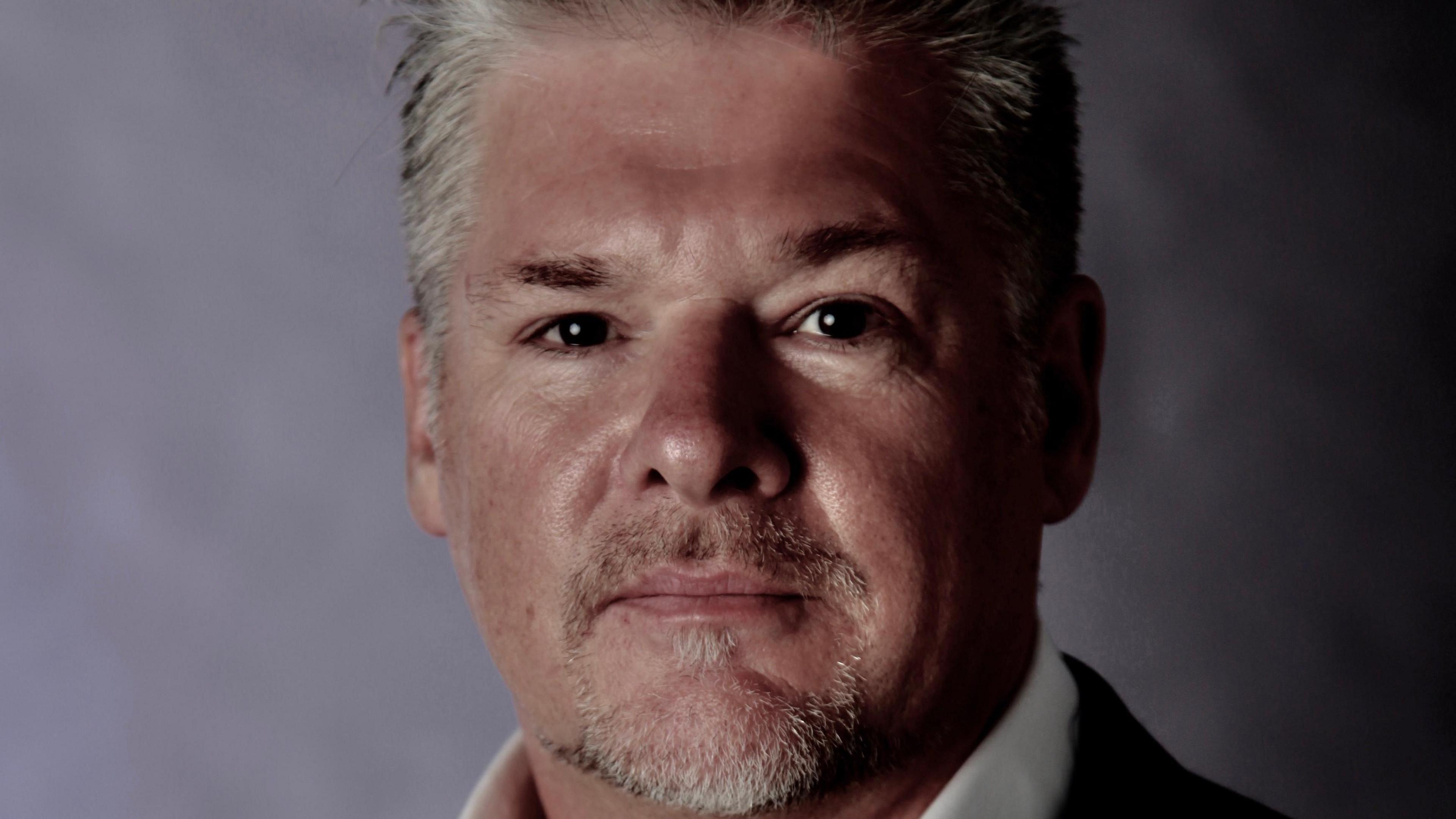 Shaun Hughes in a suit pictured against a photography studio backdrop.