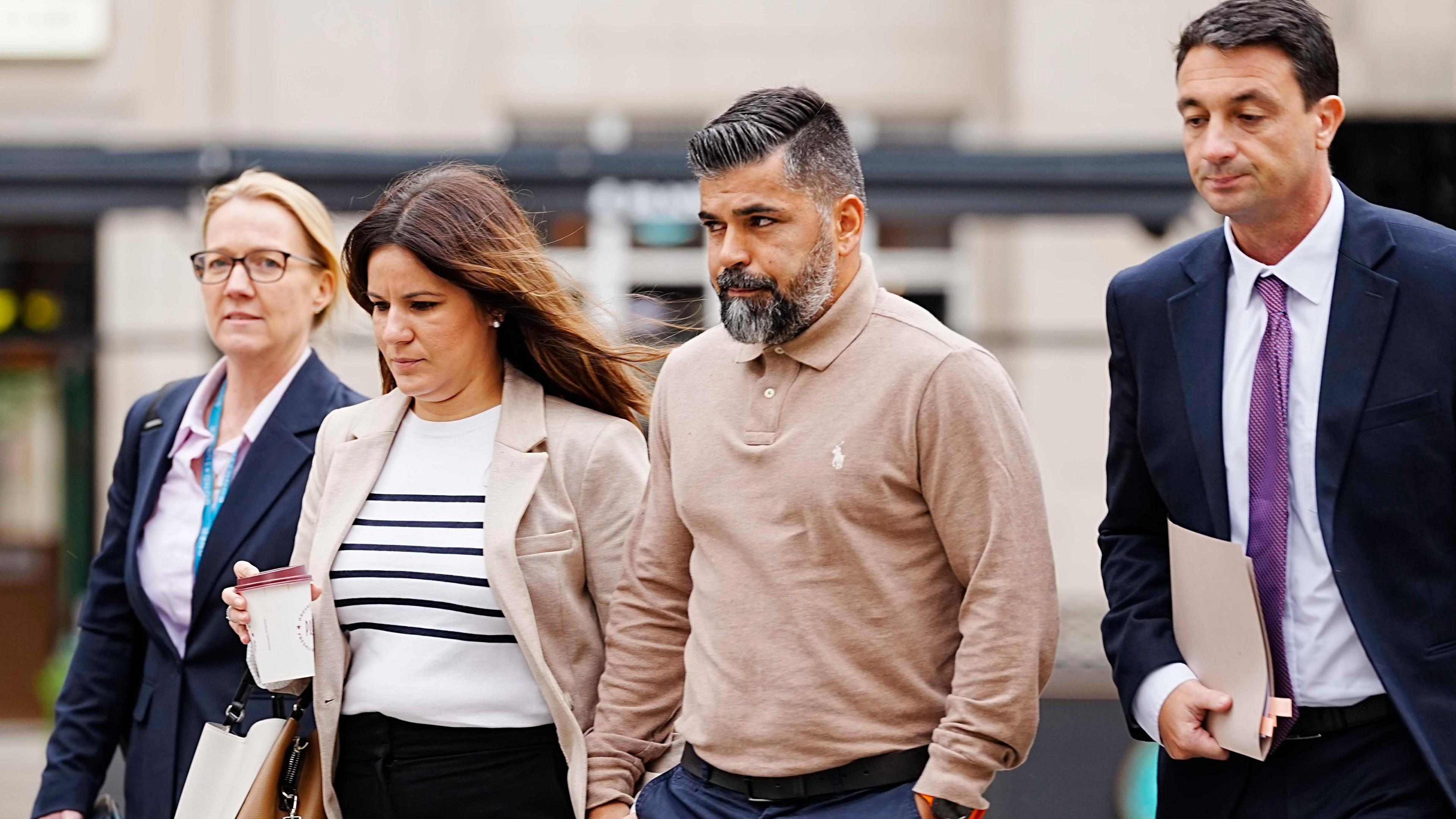 Alexandra and Sergio Aguiar walk hand-in-hand flanked on either side by their legal representatives, a woman and a man.