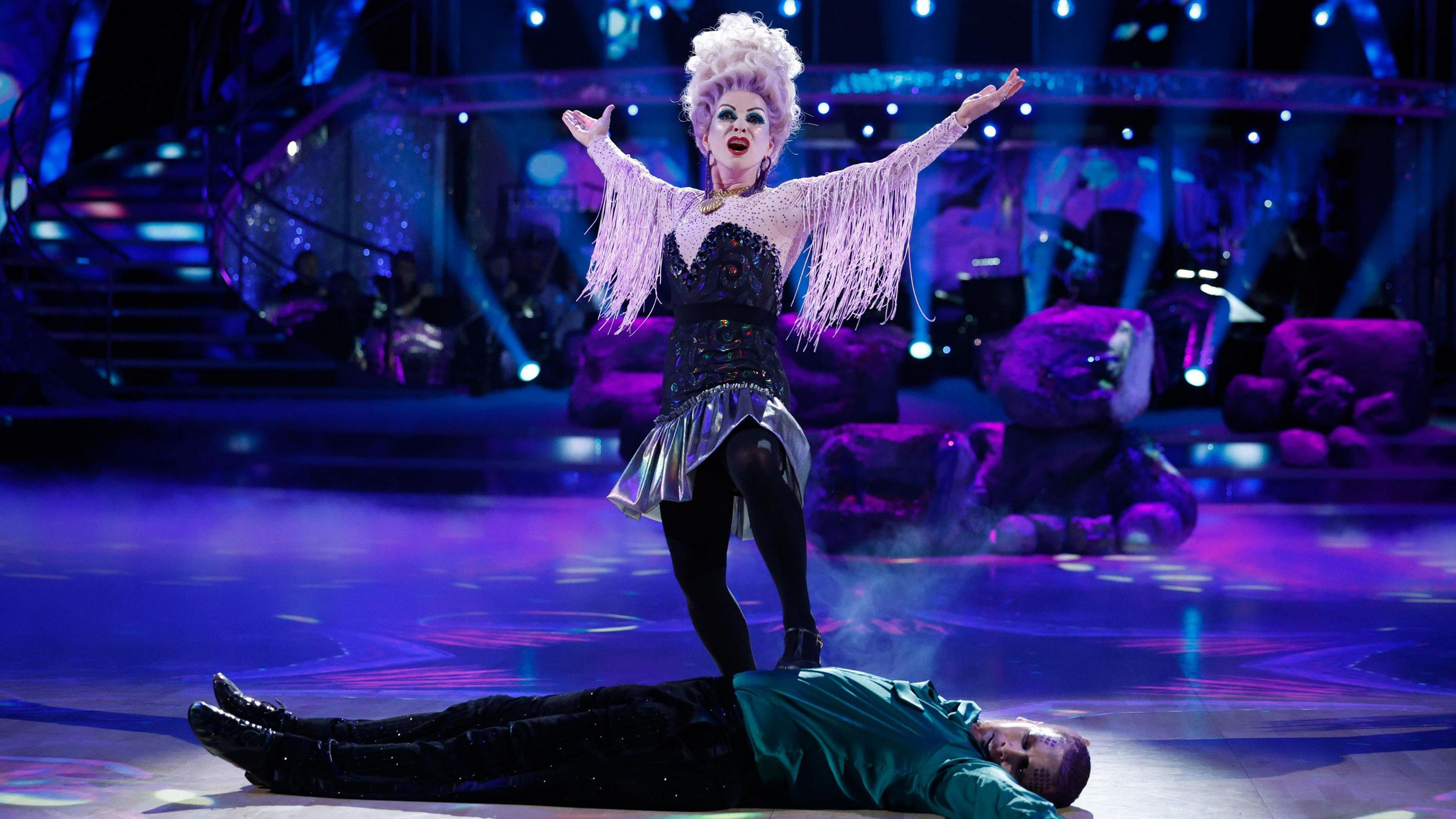 Toyah dressed as Ursula, her arms are outstretched. Neil lies on the floor as part of the dance. Strictly dancefloor.