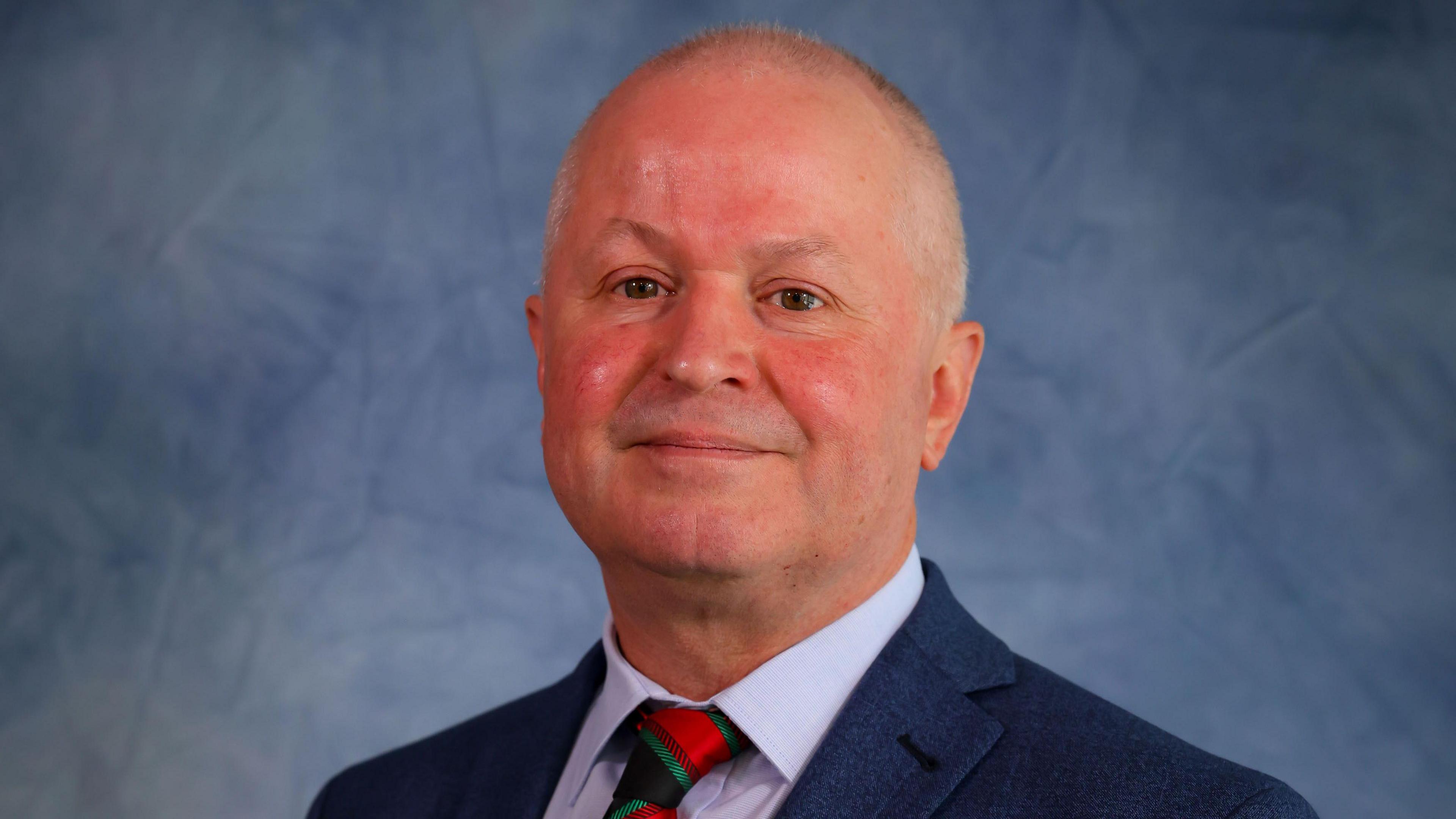 Caerphilly council leader Sean Morgan, wearing a blue suit and red and blue tie, smiling towards the camera