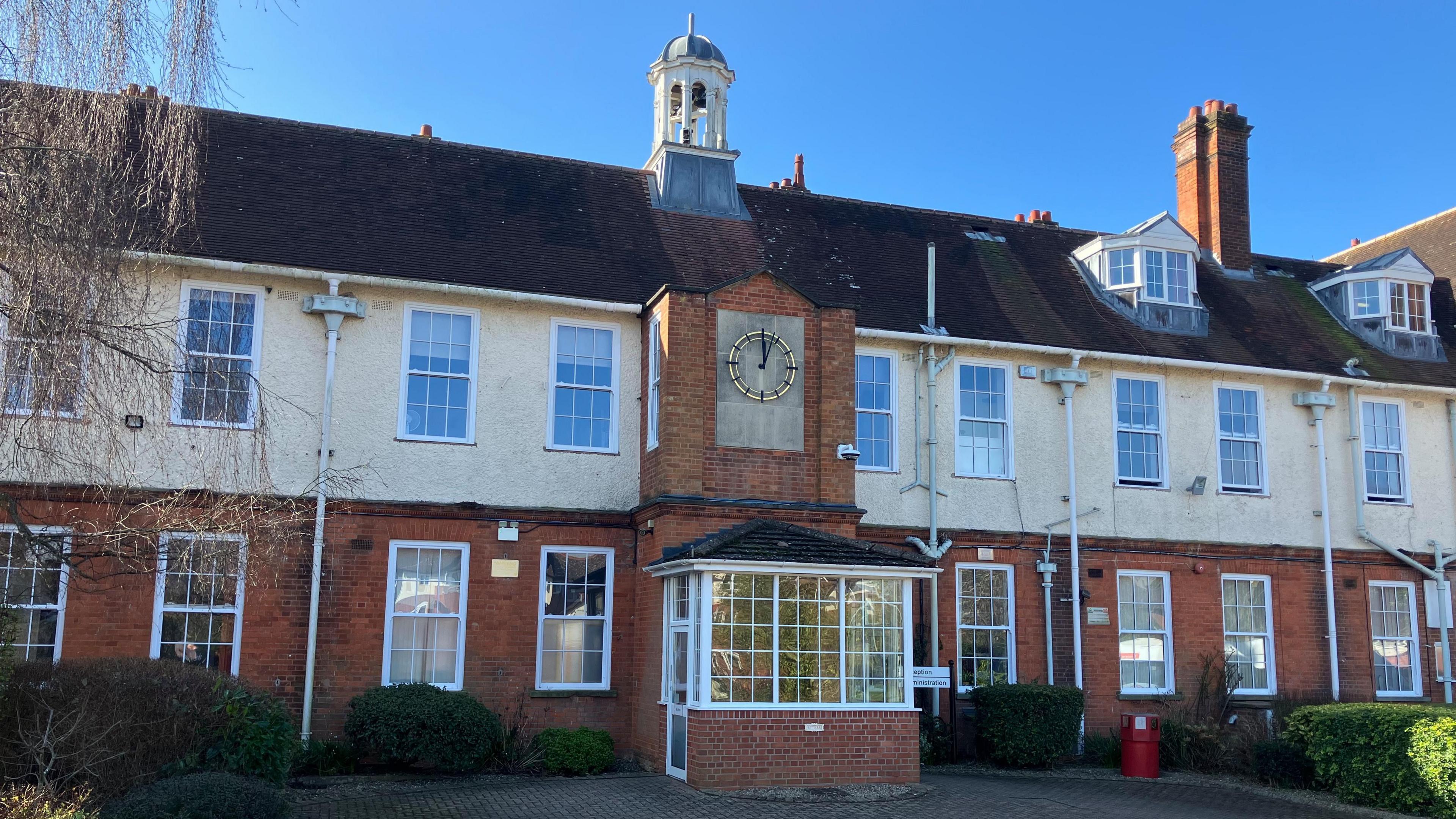 The exterior of New College Worcester. It is a long building on three storeys, with windows along its length. A clock is on the wall above what looks like the reception.