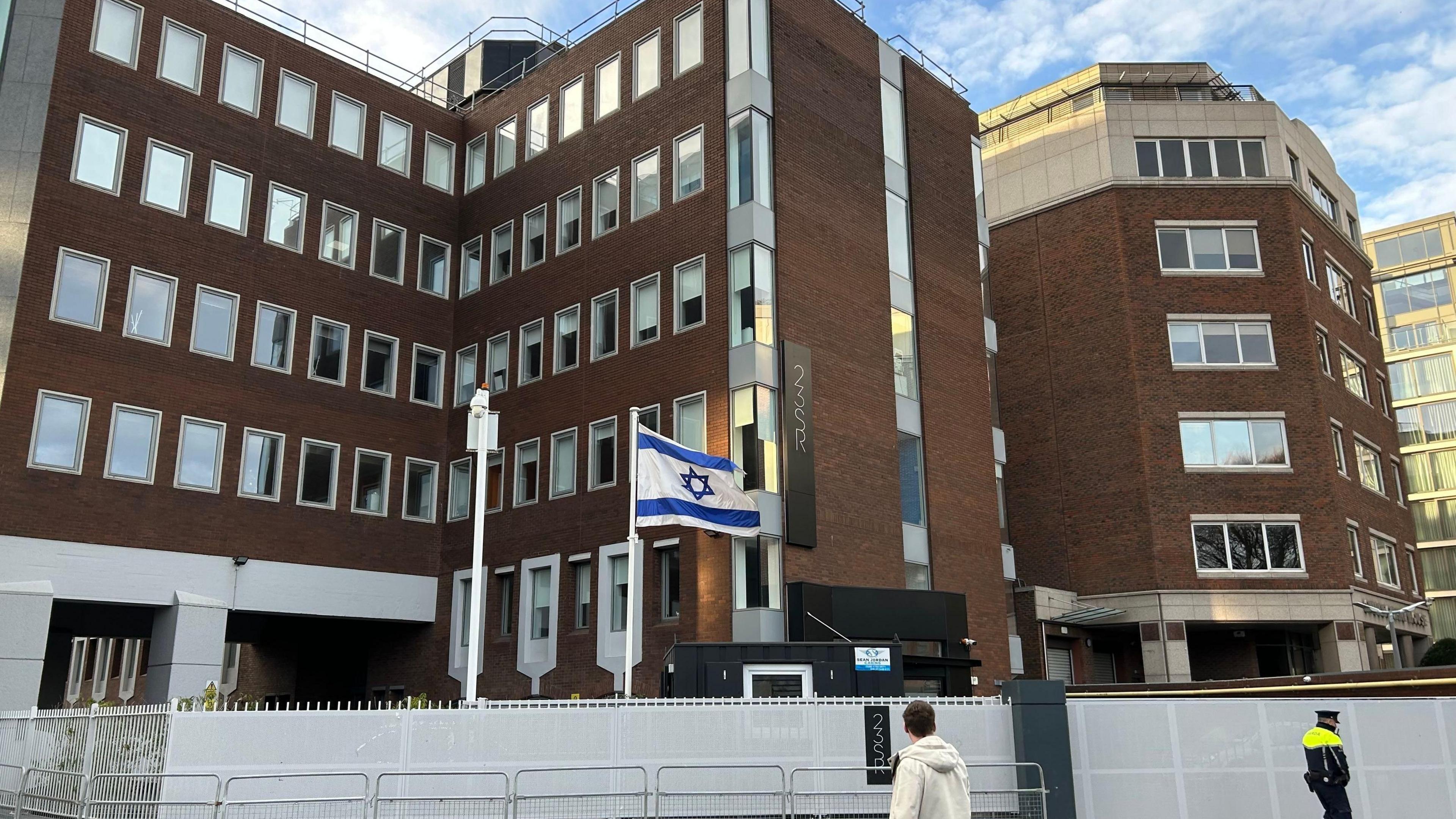 Israel embassy in Dublin, a large brown building with lots of windows, a white flag with blue star and banners is blowing in front of building