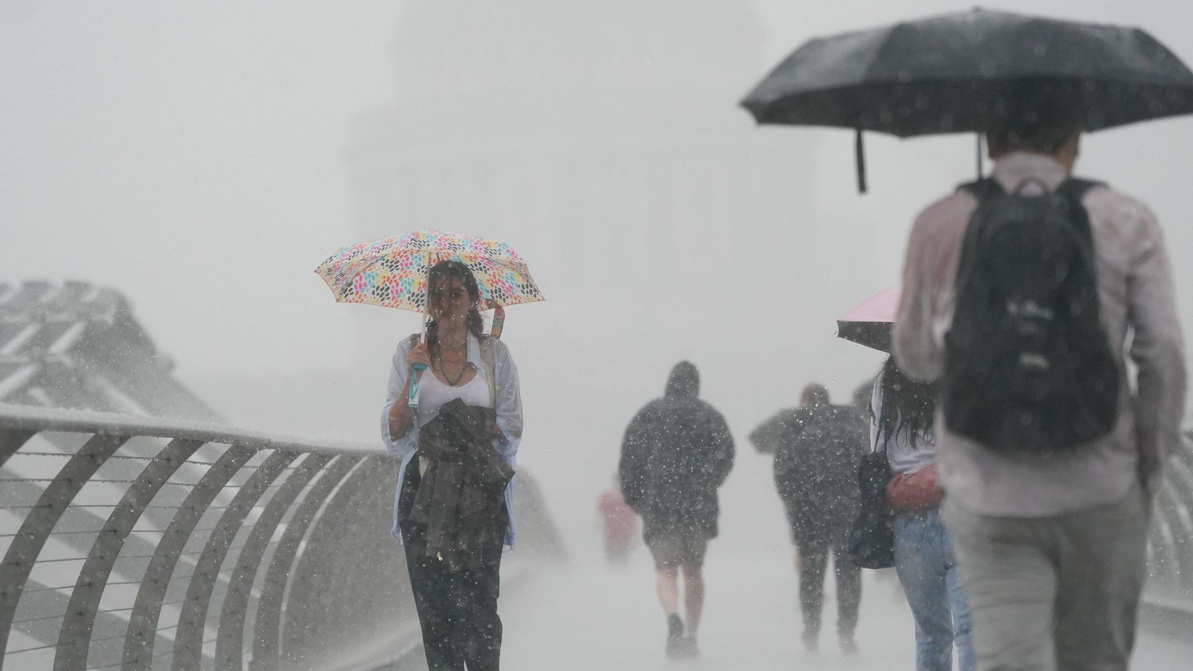 People walk across Millennium Bridge in torrential rain
