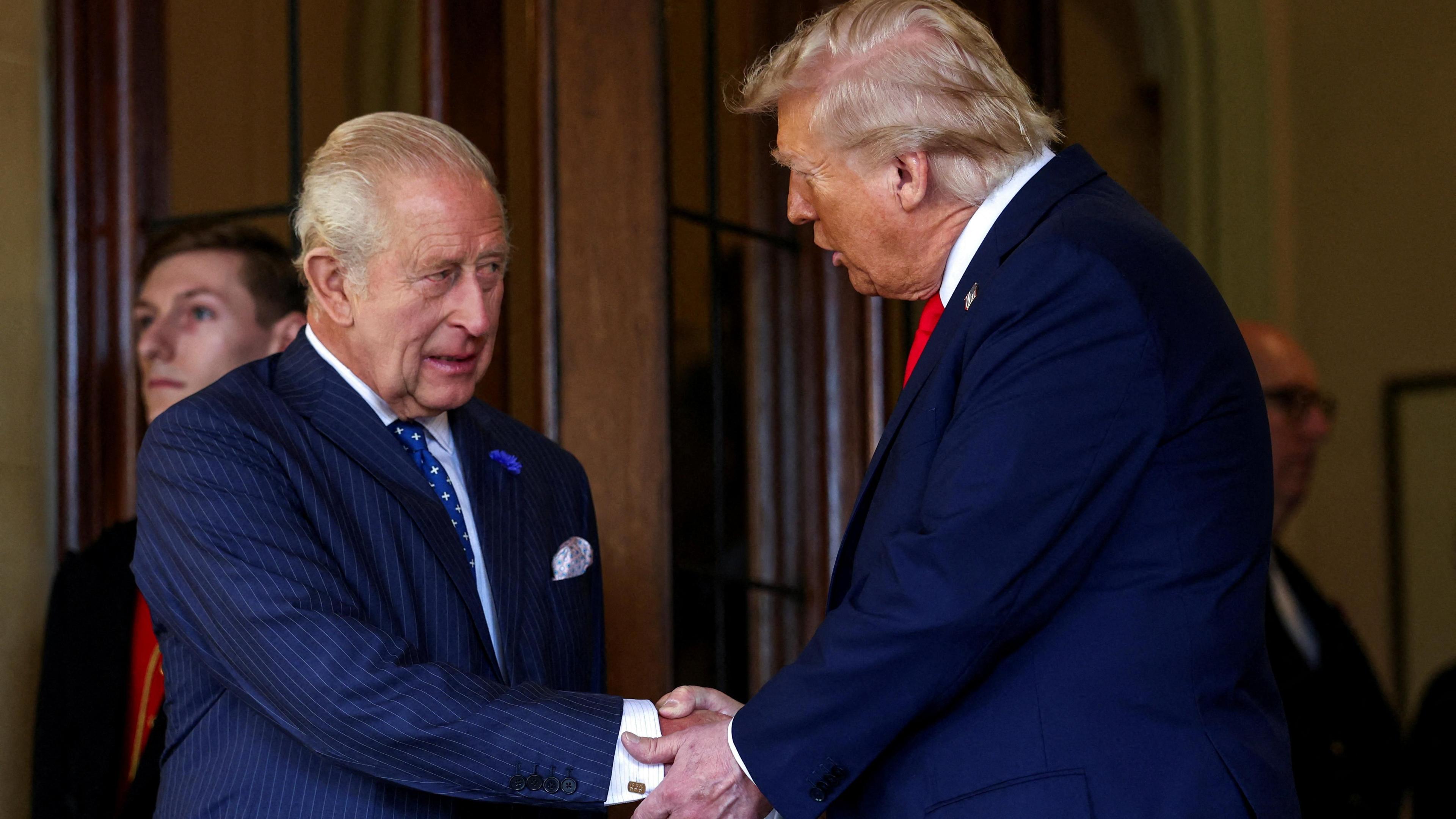 A man in a blue pin-striped suit is shaking the hand of another man in a navy blue suit, who is also wearing a red tie.
