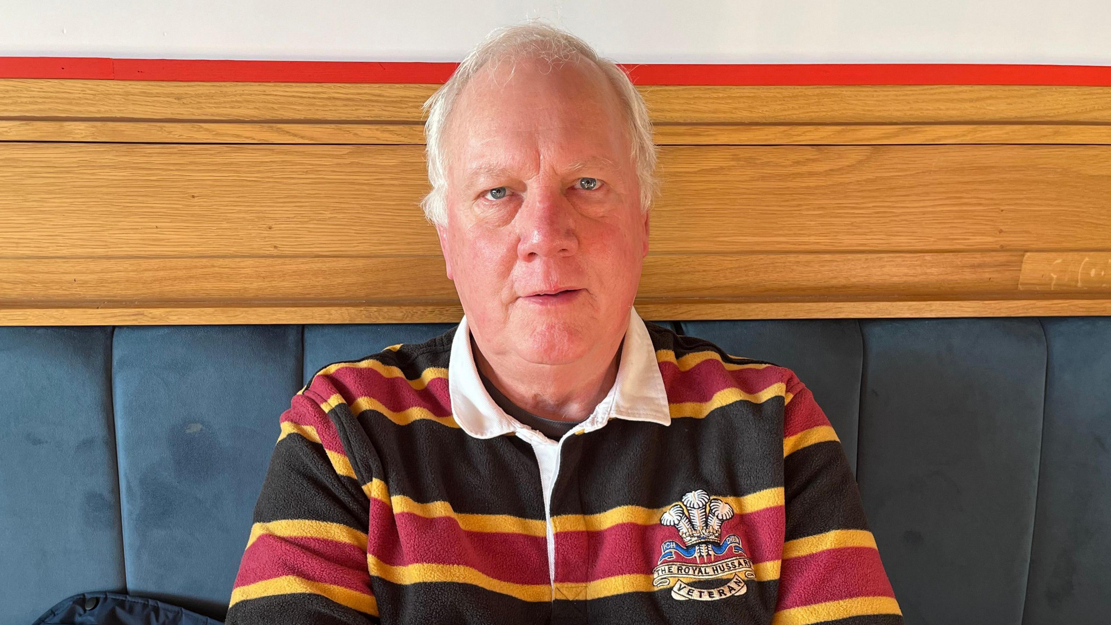 A man with grey hair is wearing a blue, yellow and red striped rugby shirt.
