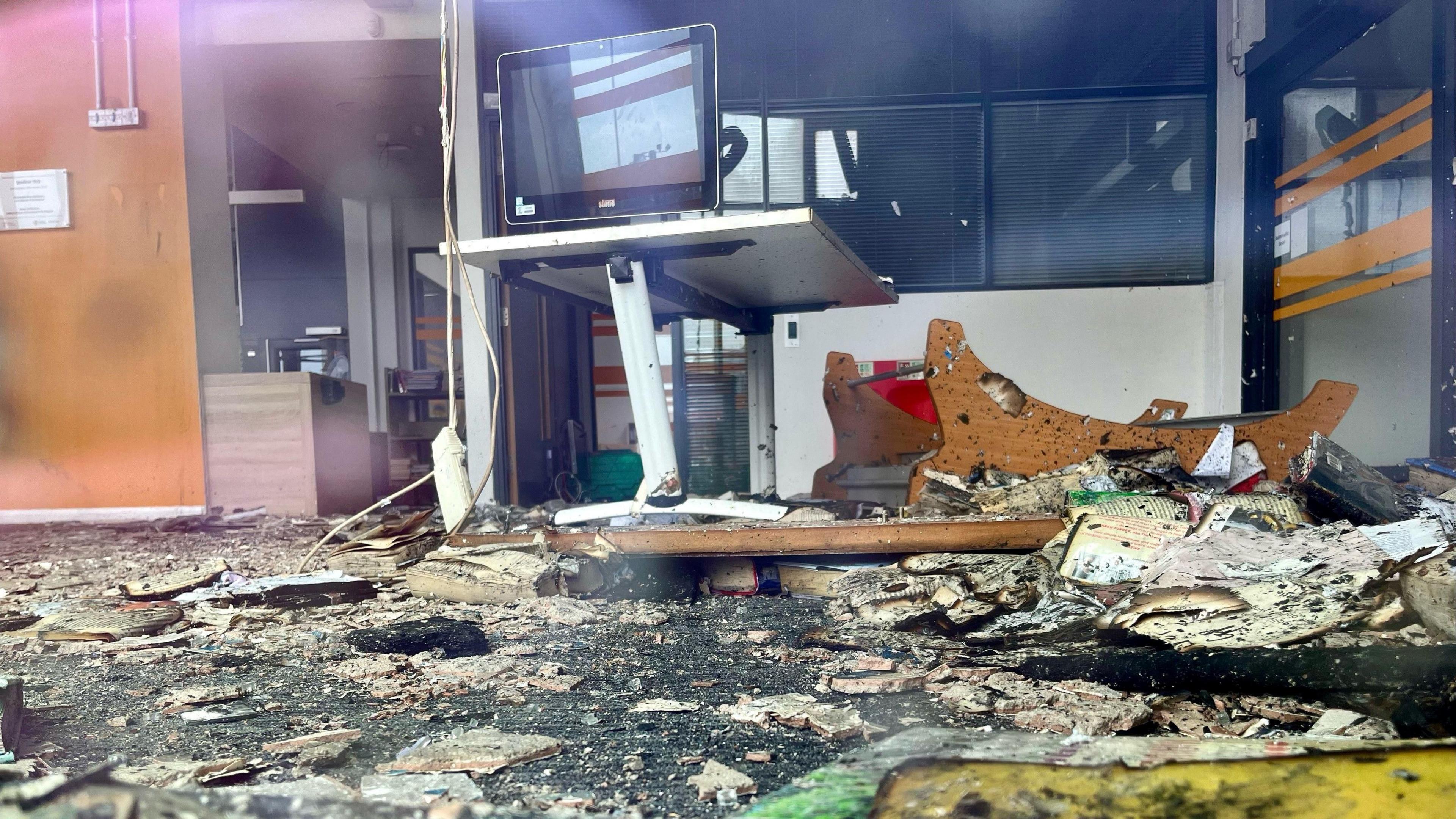 The destroyed interior of the Spellow Hub community library. A computer screen on a stand is the last remaining furniture with debris all over the floor.