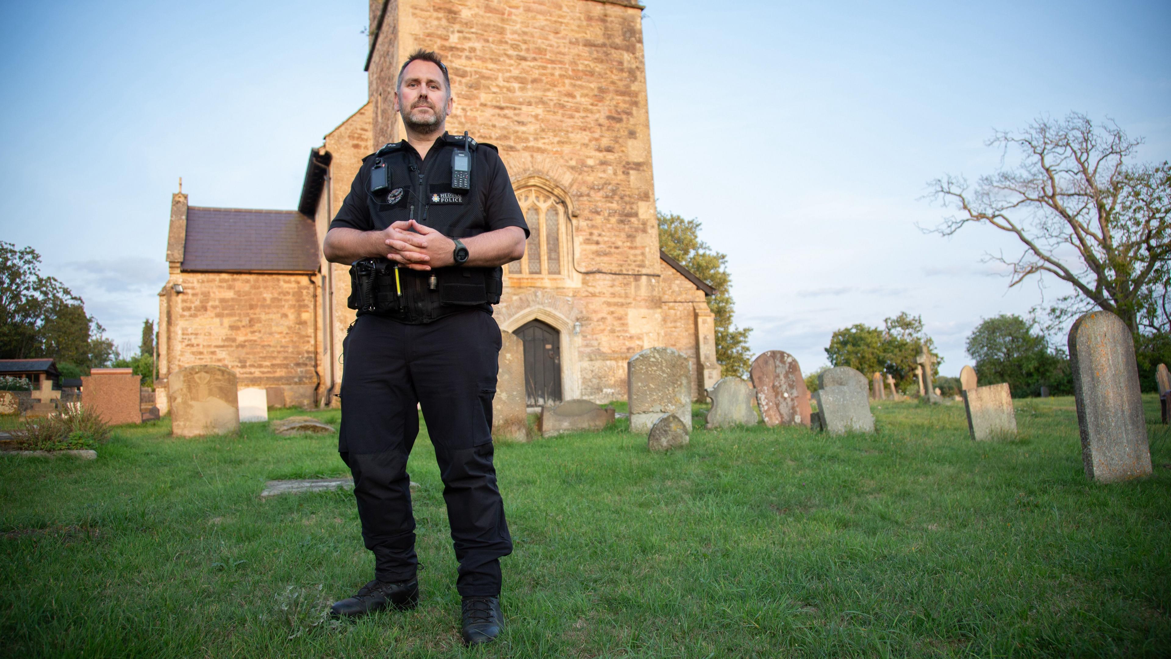 PC Dan Counsell o Heddlu Gwent mewn mynwent lle cafodd degau o dyllau wedi eu cloddio eu darganfod